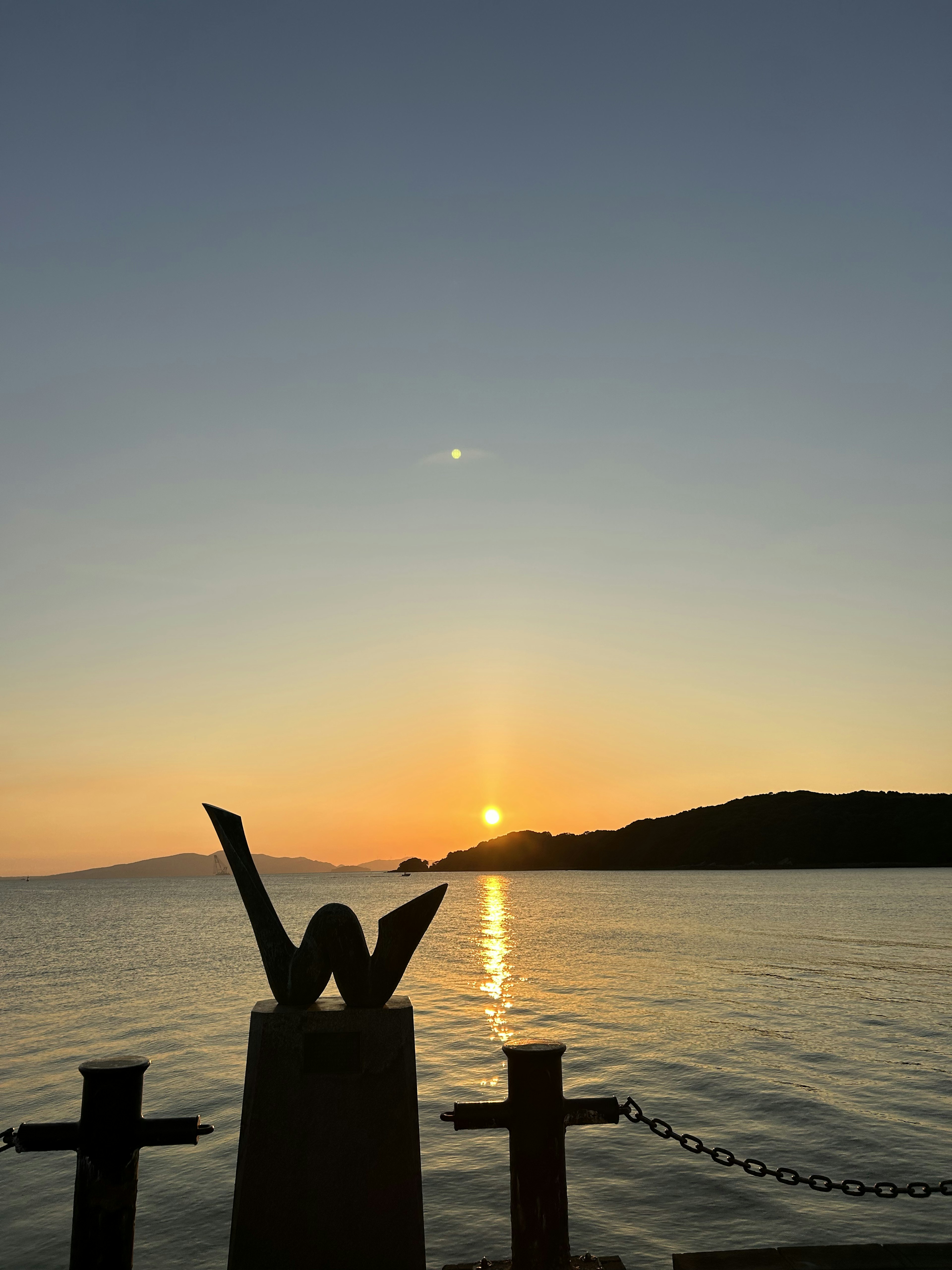 夕日が沈む海の風景とシルエットの彫刻