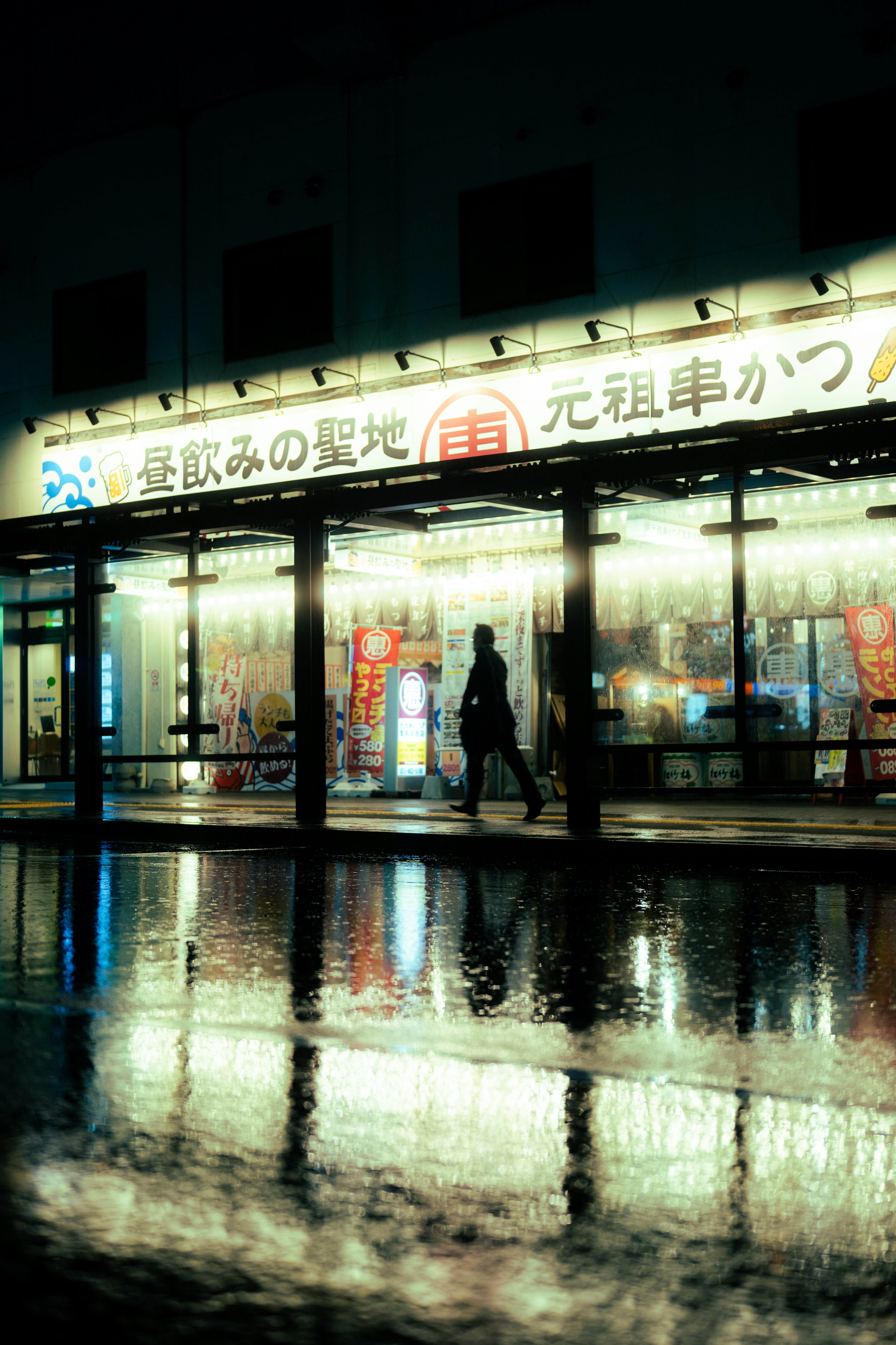 Night scene of a storefront with reflections in puddles during rain