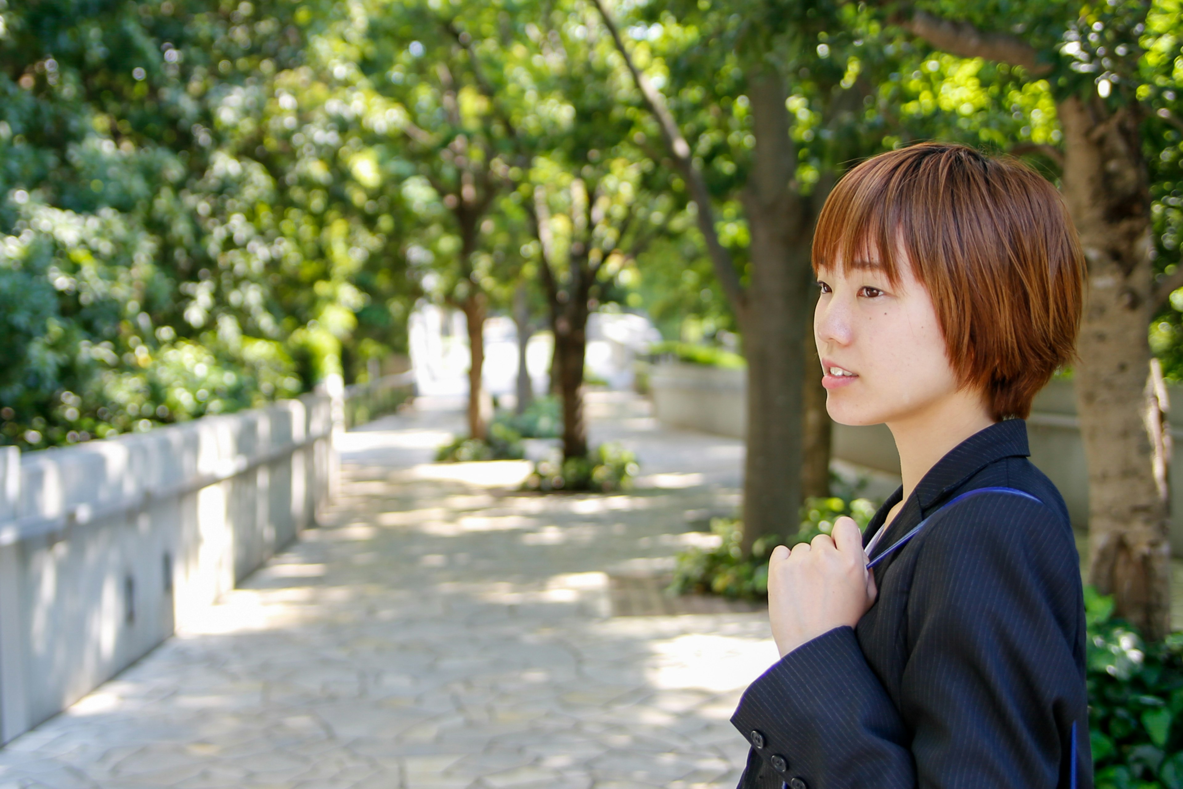 Profile of a woman standing on a tree-lined path