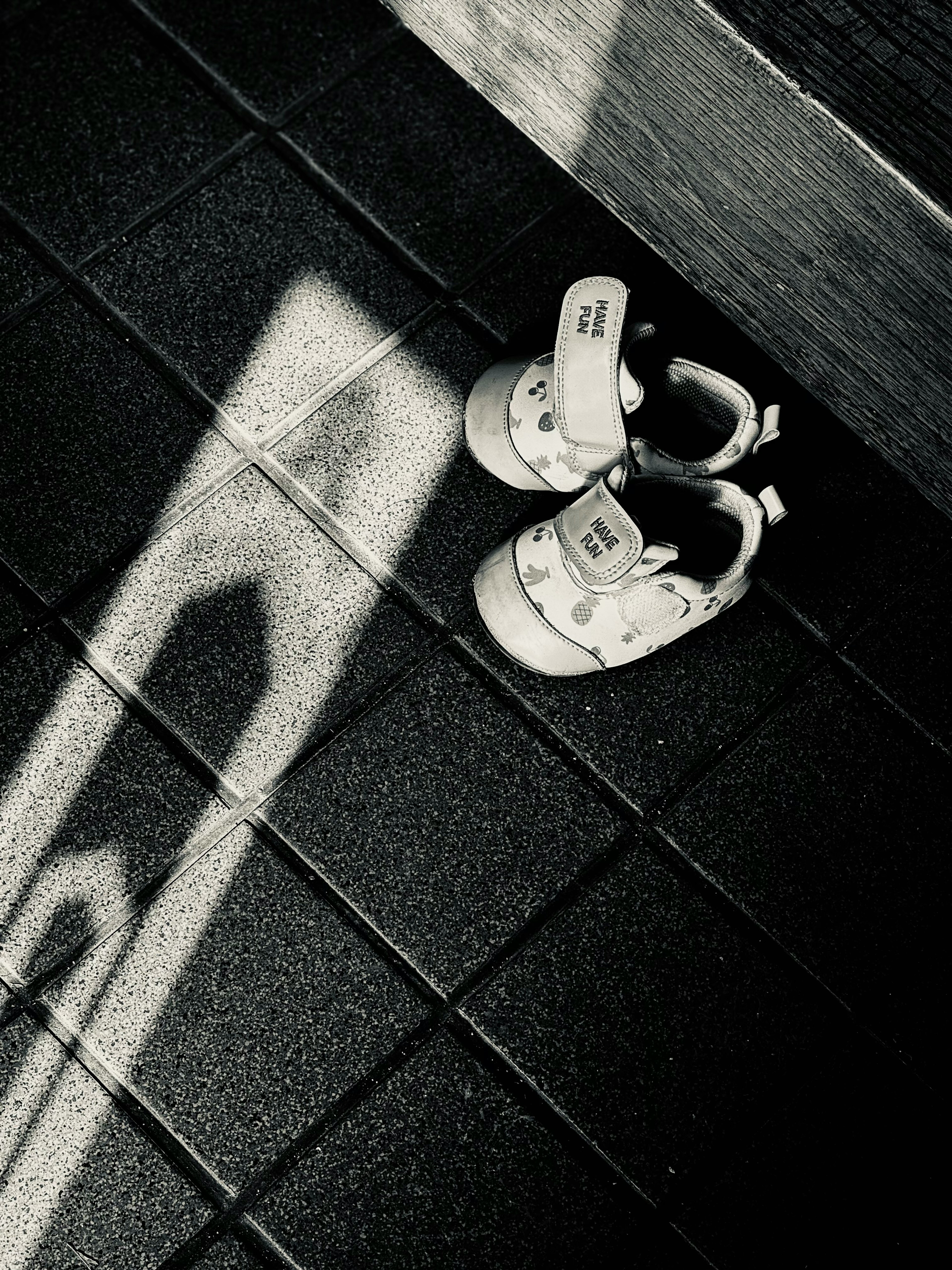 Weiße Babyschuhe auf schwarzen Fliesen mit einem Schatten