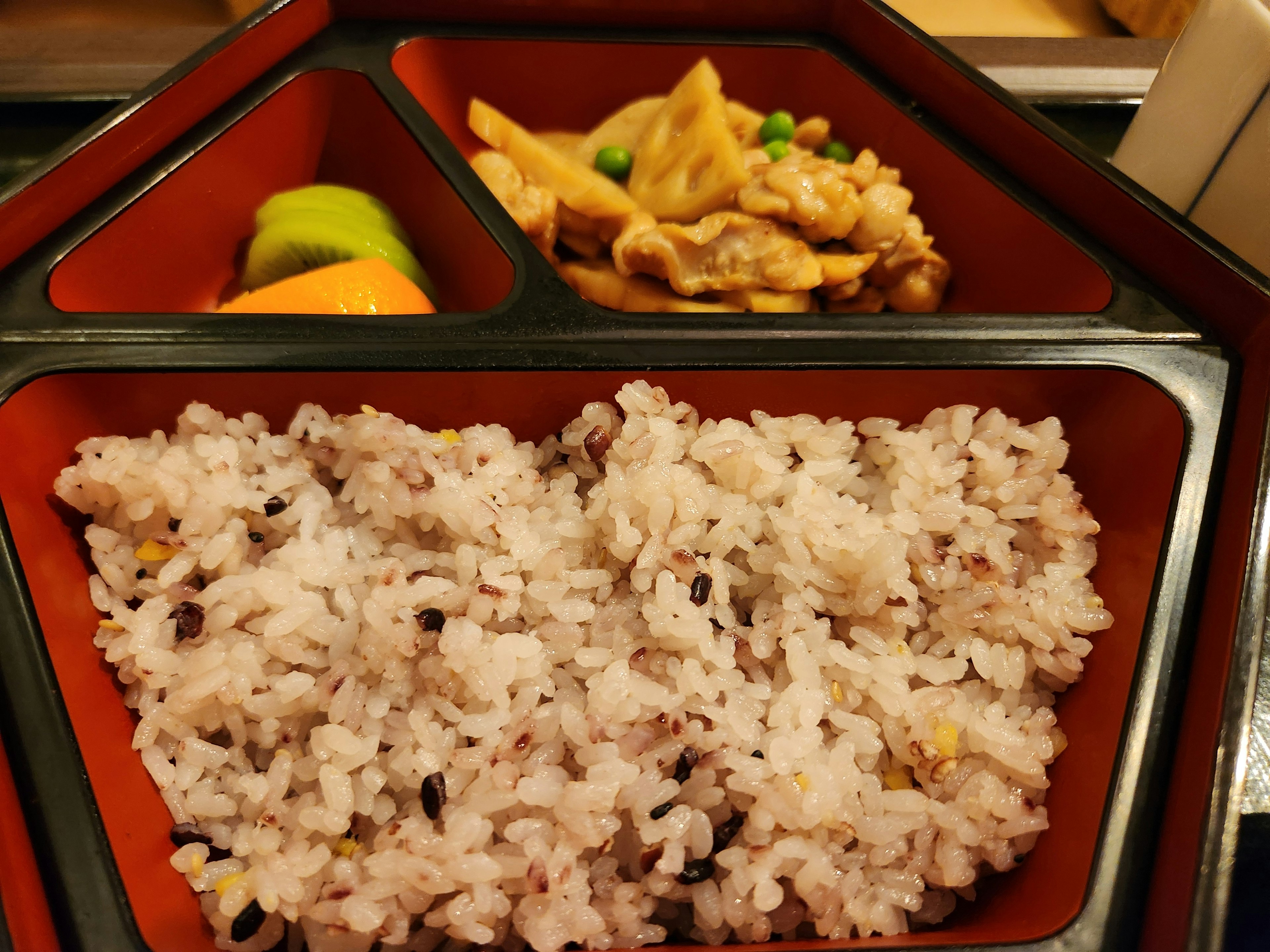 A red bento box containing mixed grain rice and chicken dish