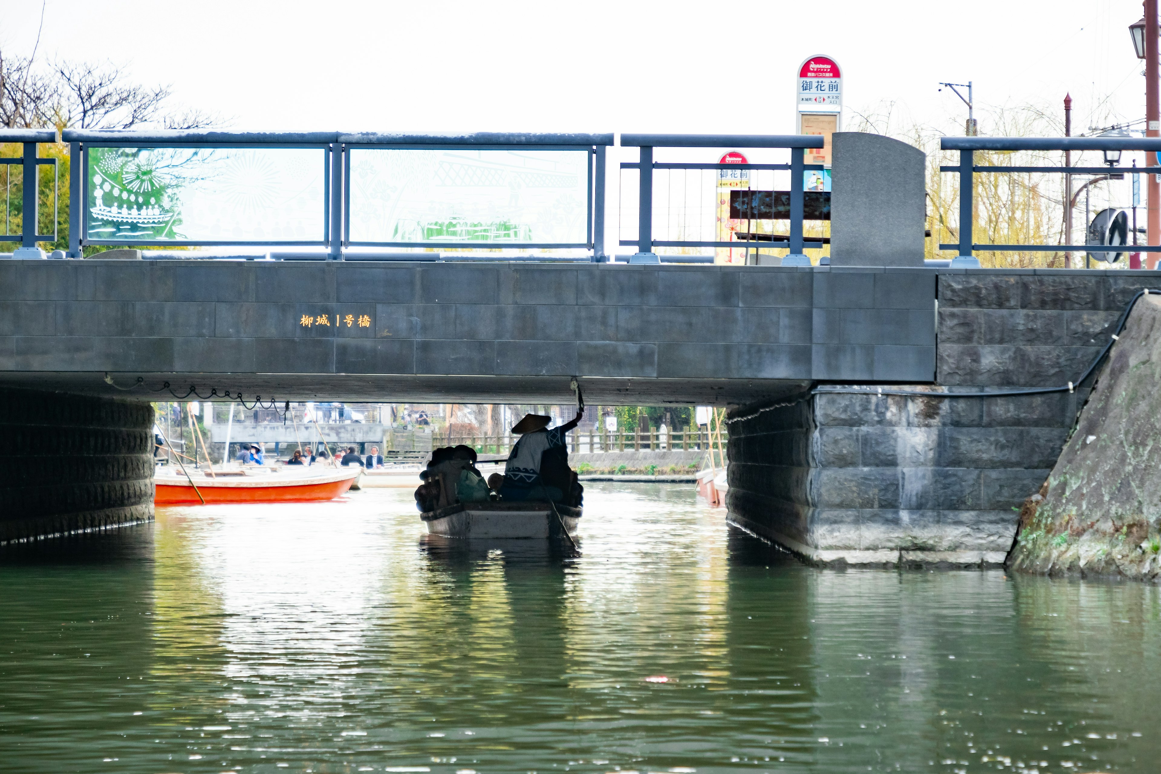 Perahu kecil melintas di bawah jembatan dengan permukaan air tenang