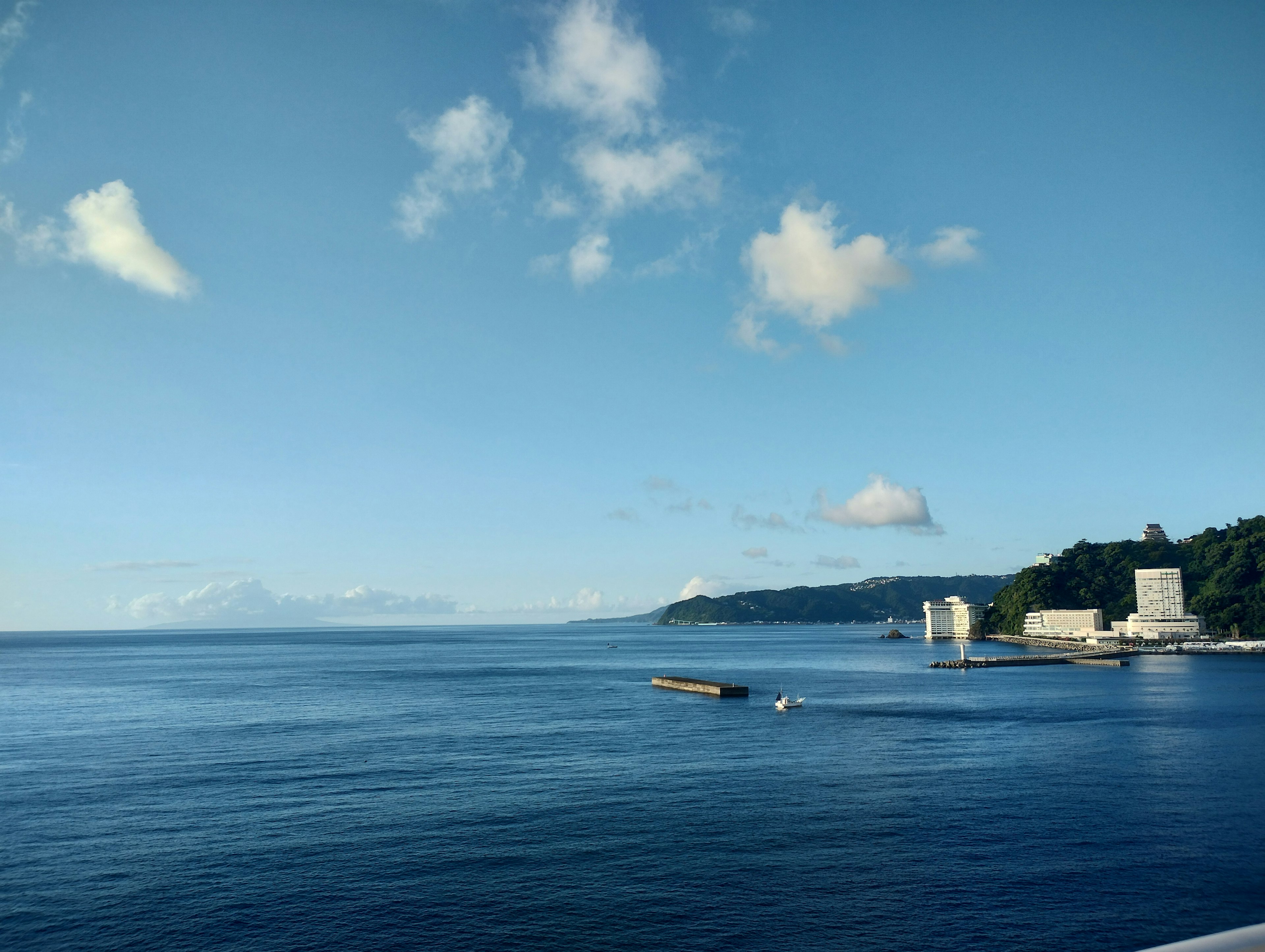 Pemandangan laut biru dan langit dengan bangunan pesisir dan ombak lembut