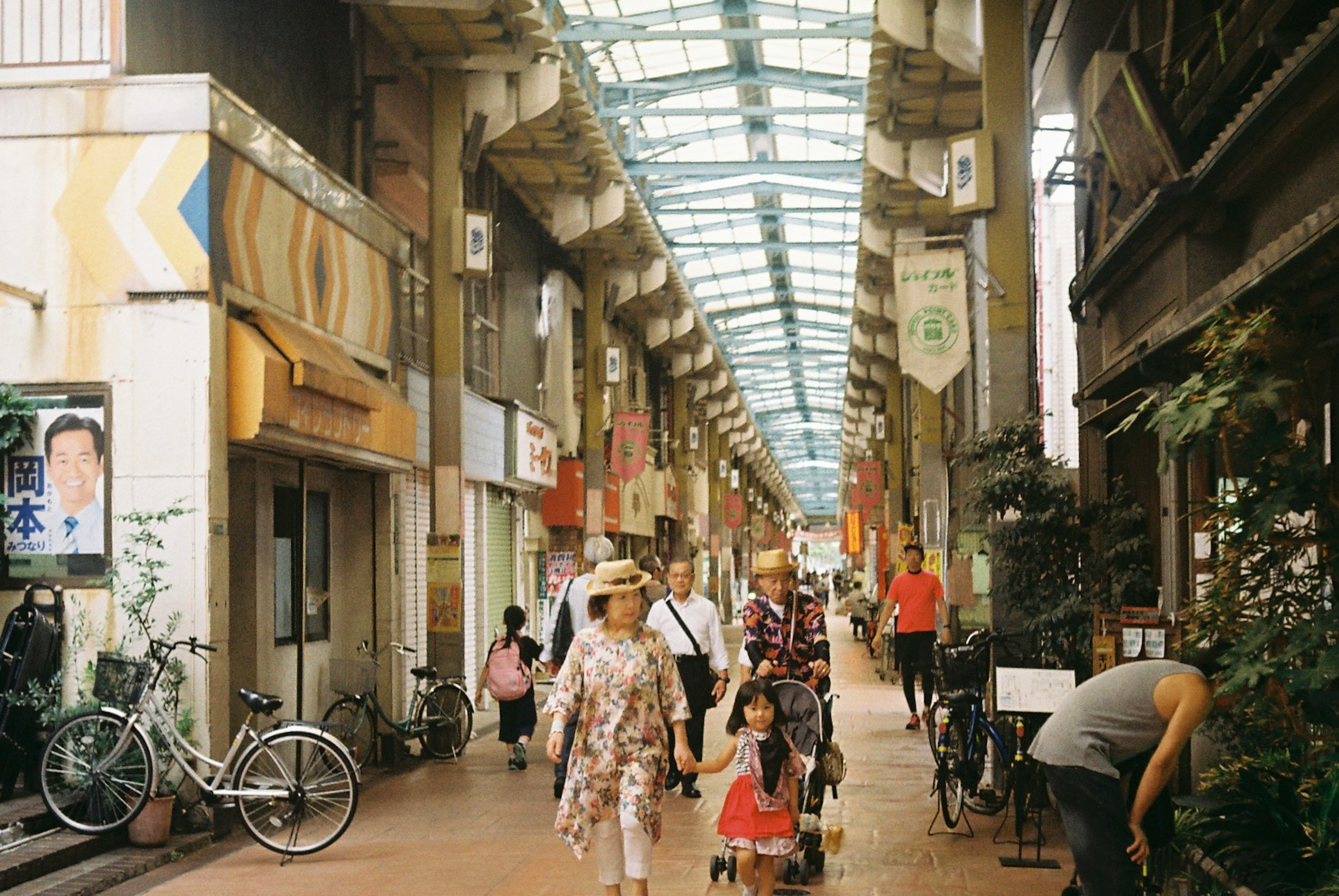 Busy shopping arcade with people walking bicycles and storefronts lining the sides