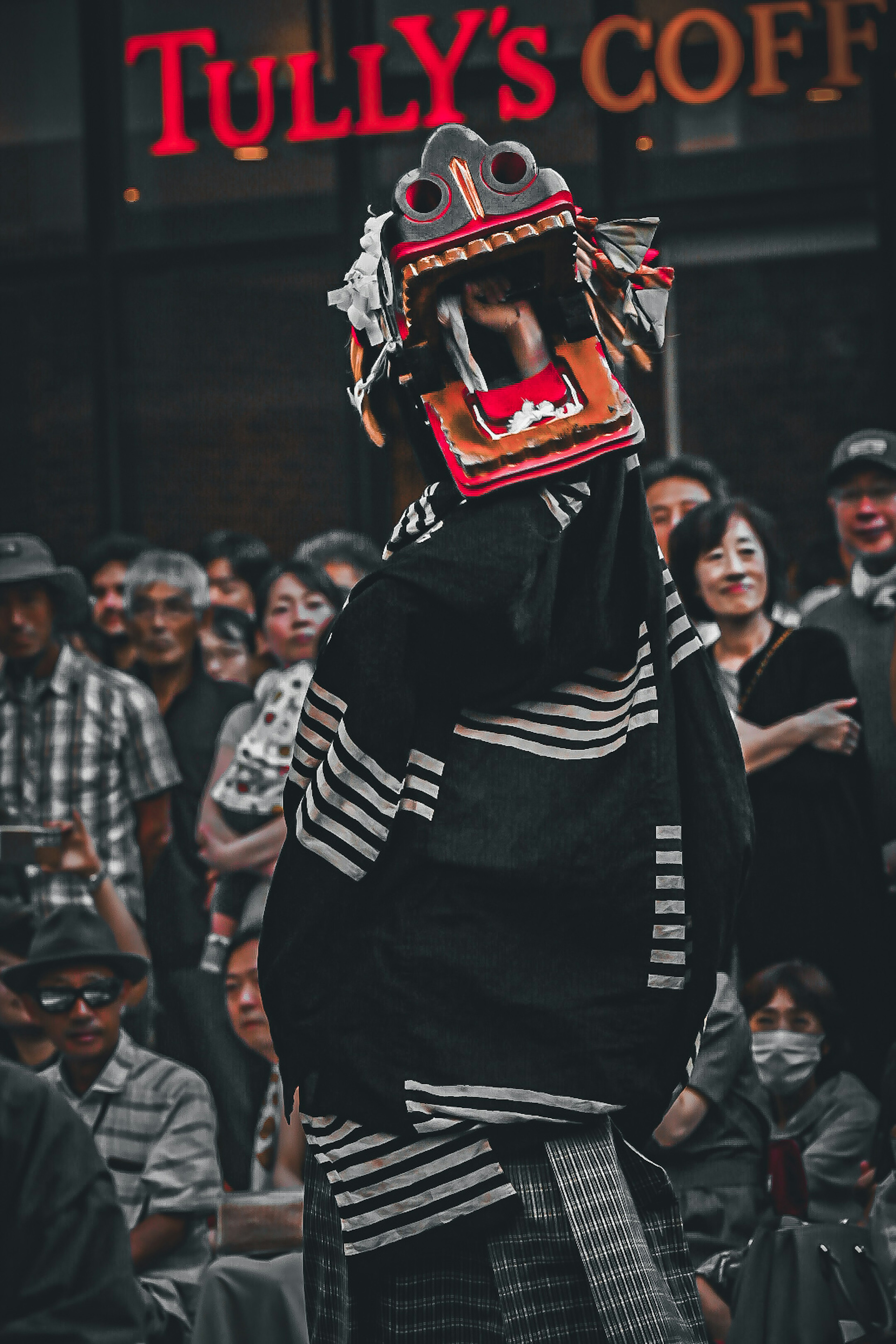 Darsteller in traditioneller Kleidung mit einer Löwentanzmaske vor einem Publikum