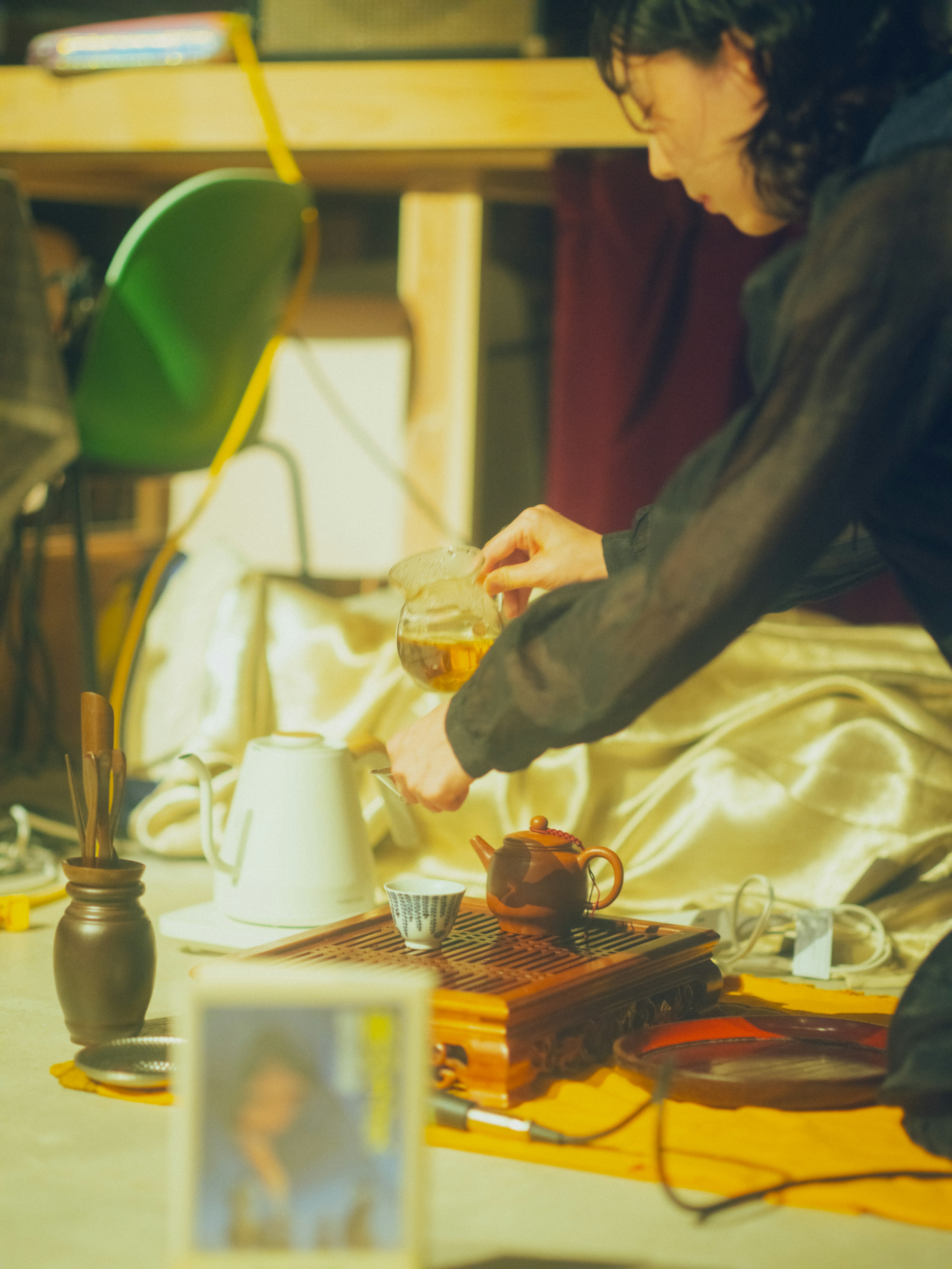 Una mujer sirviendo té con utensilios tradicionales en una mesa con una tetera y una foto