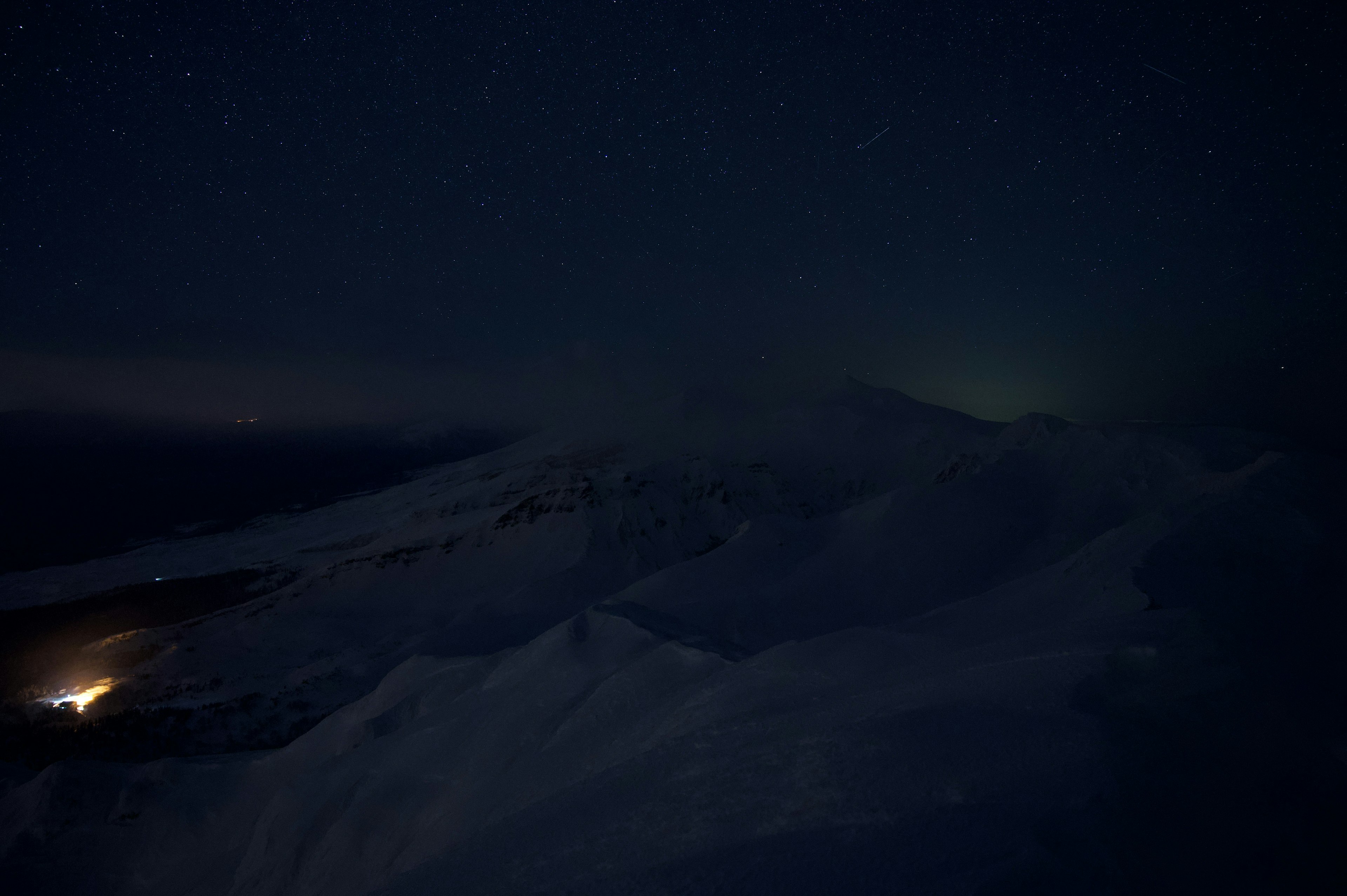 Snowy mountain landscape under a starry night sky with a small light source