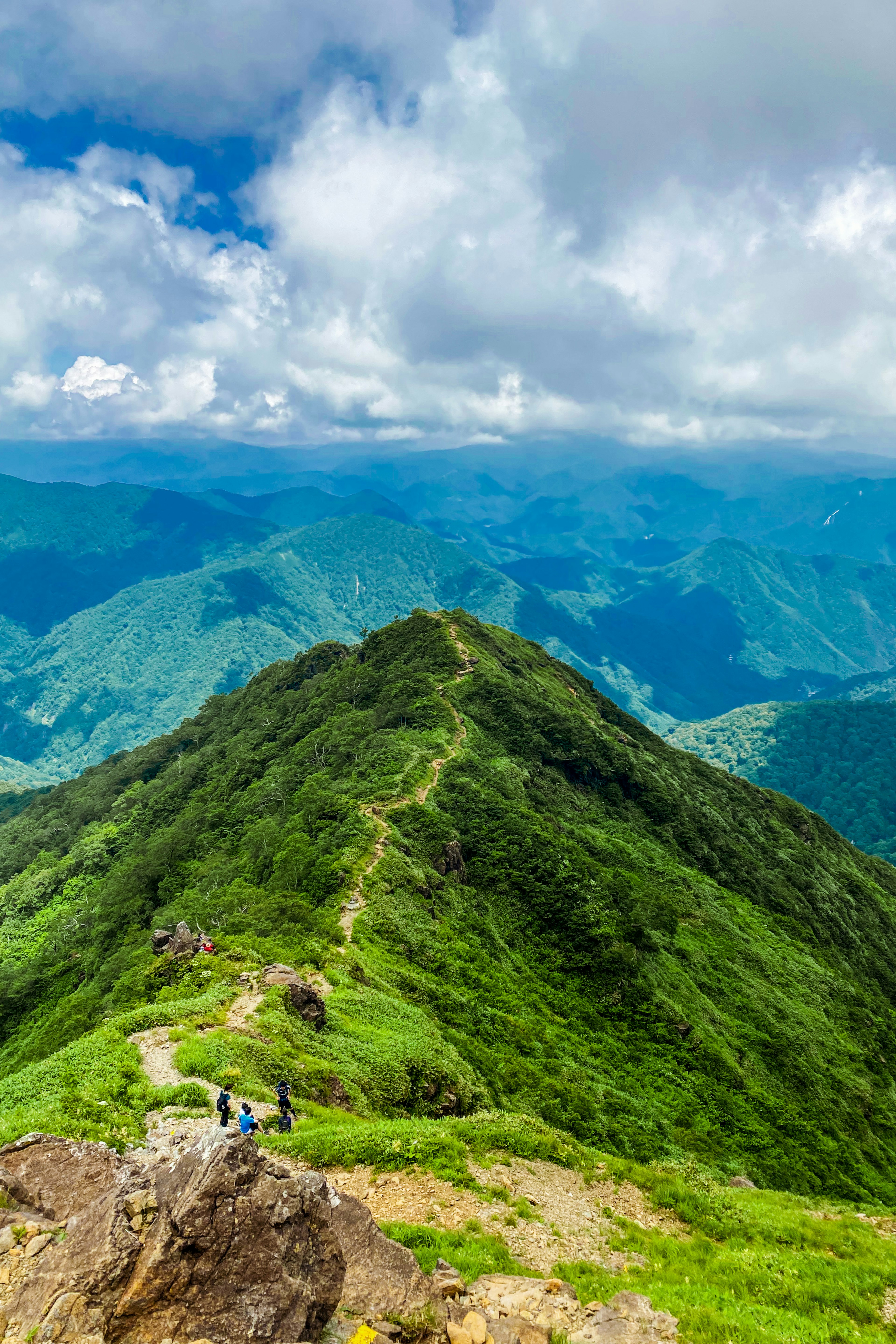 Vue panoramique depuis un sommet de montagne montrant une végétation luxuriante et des montagnes lointaines