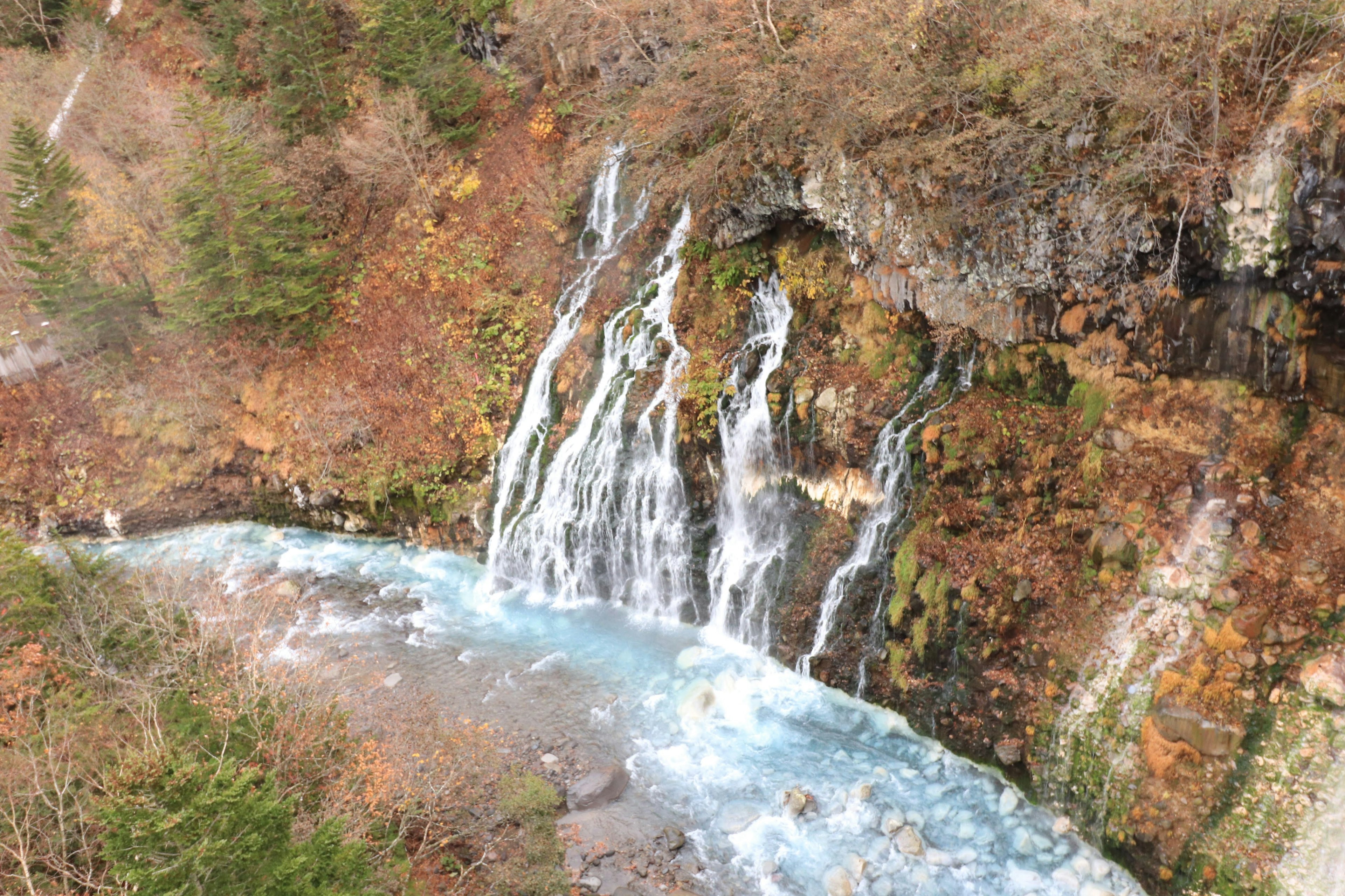 Air terjun yang indah mengalir dikelilingi pohon hijau dan oranye