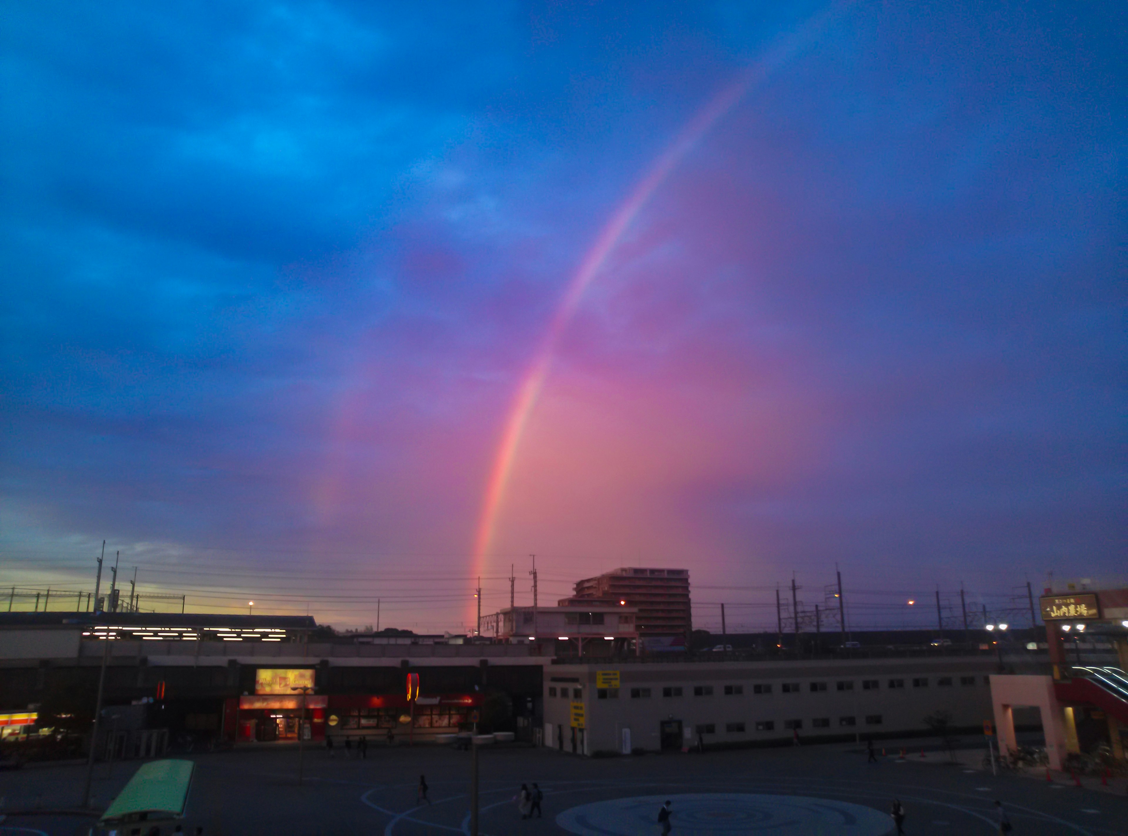 Arcobaleno che si estende su un cielo di tramonto colorato con silhouette di edifici