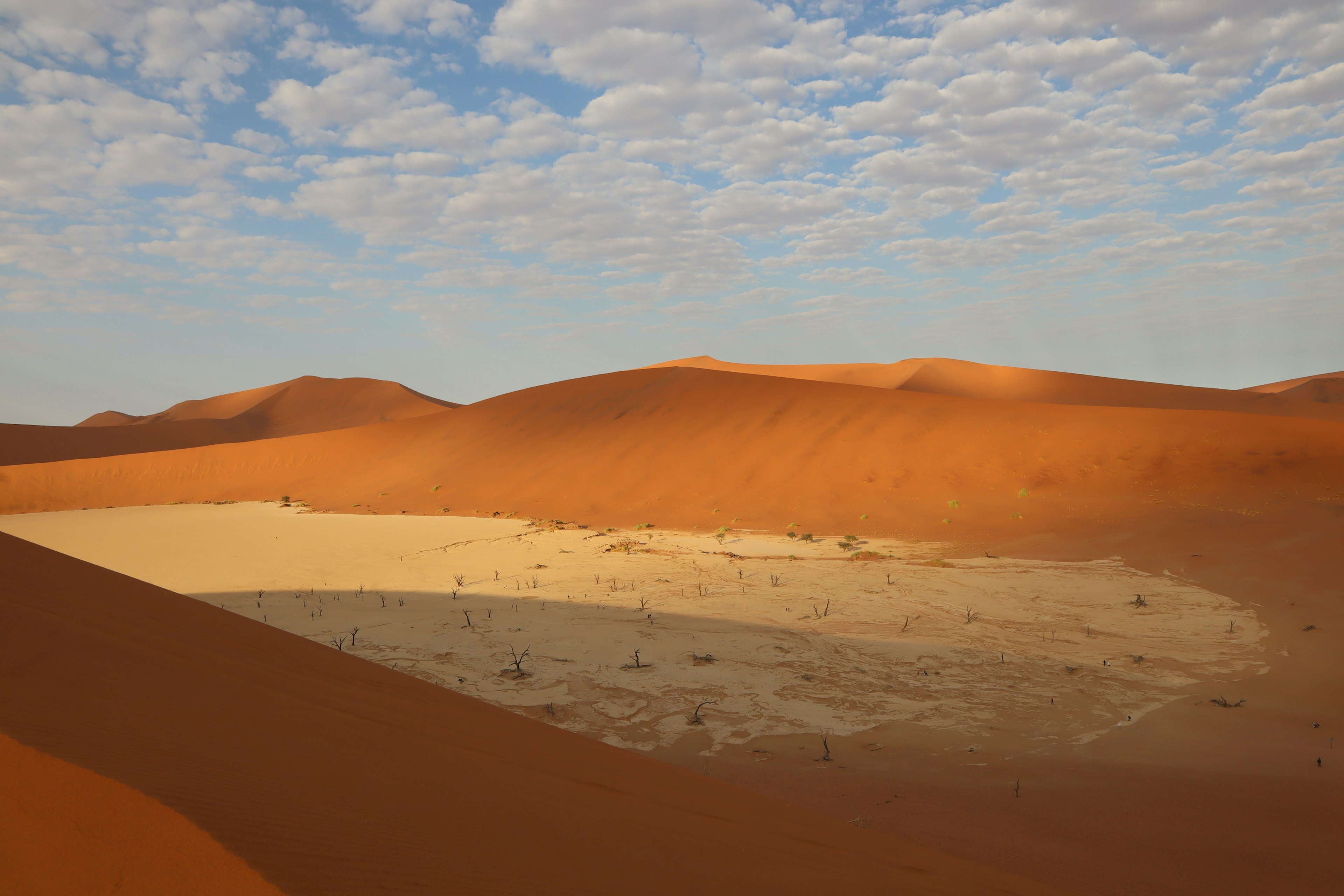 Amplio paisaje desértico con dunas de arena naranja y un cielo azul con nubes