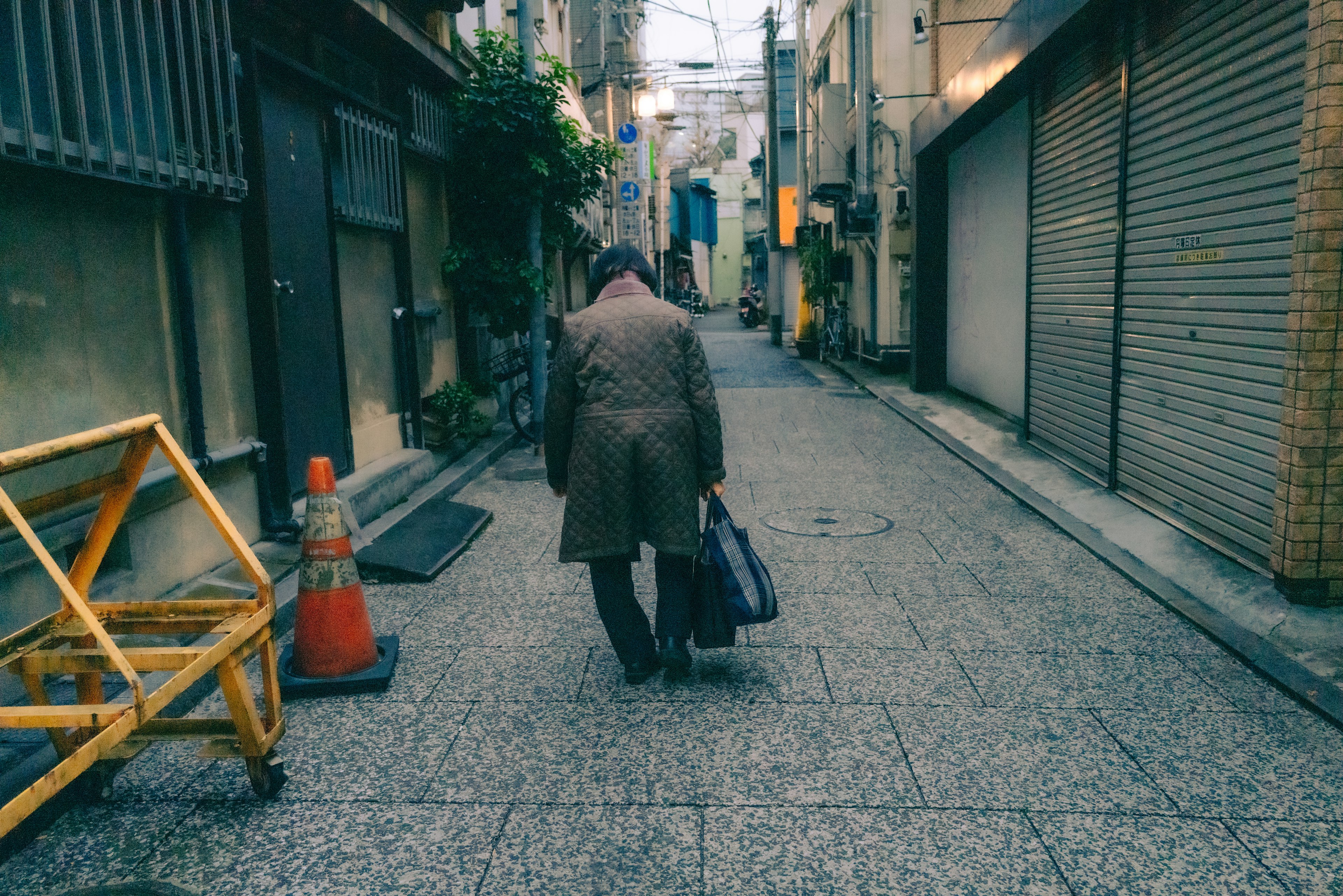 A man walking down a narrow alley with closed shop shutters