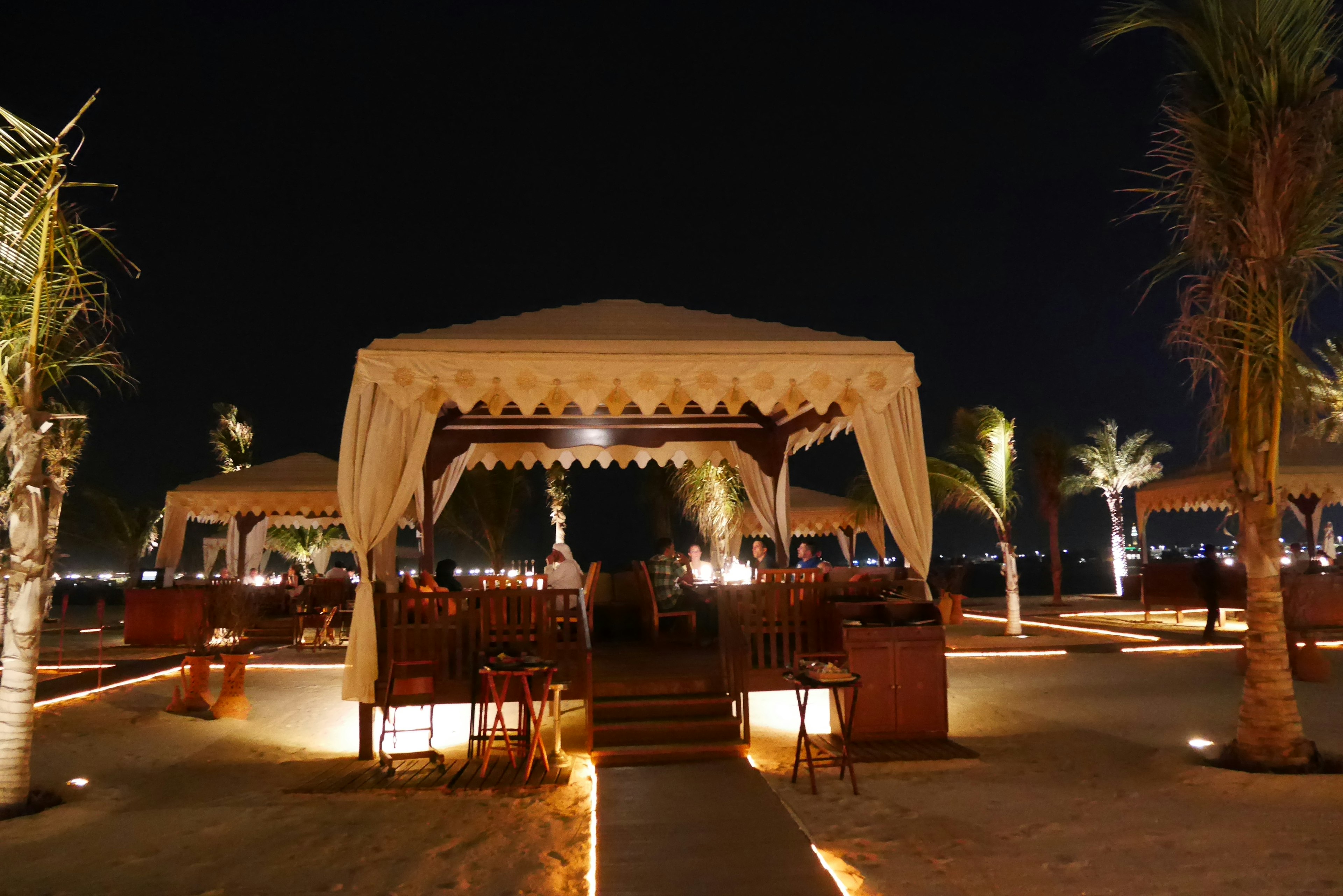 Beach restaurant tent illuminated at night with palm trees