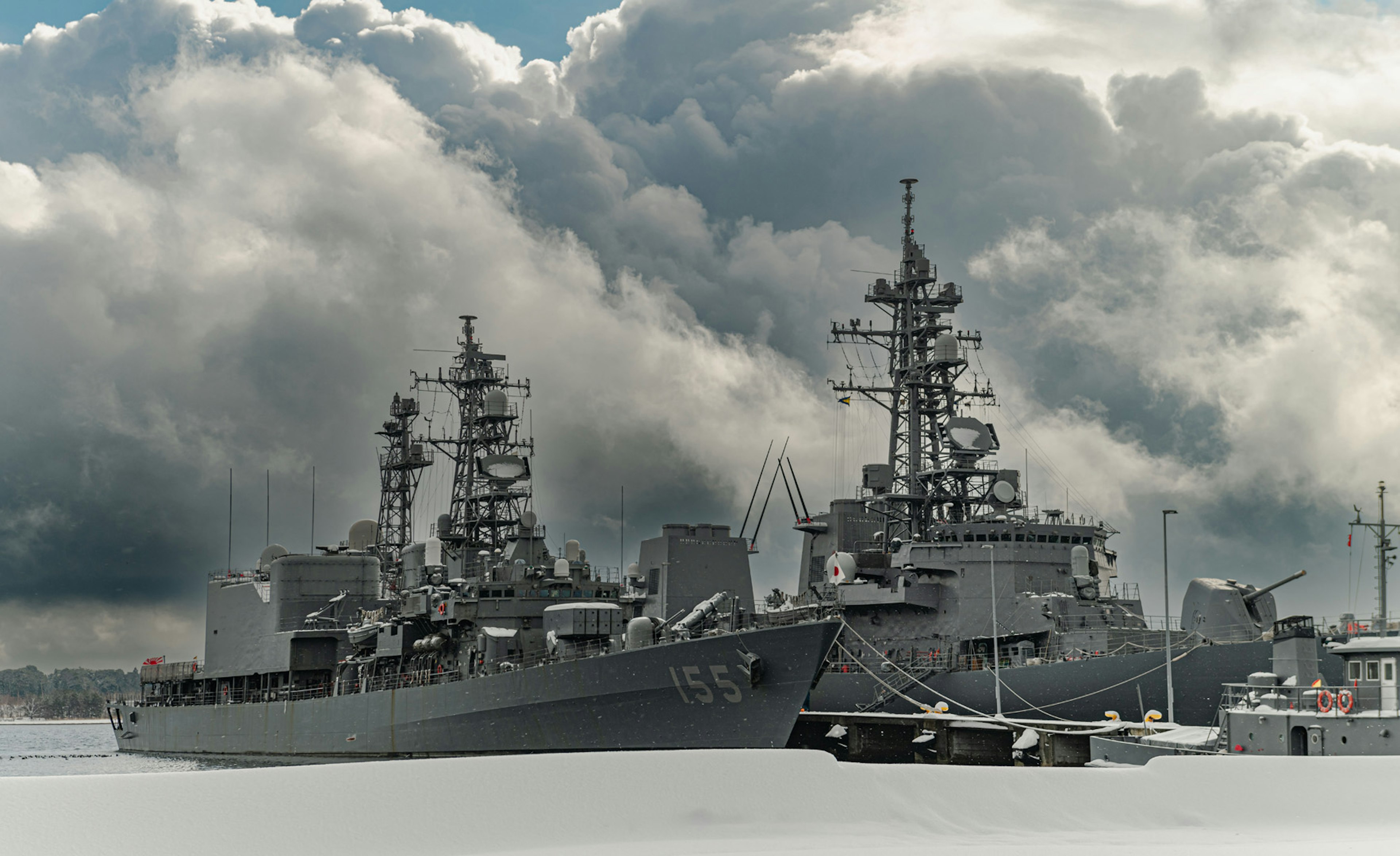 Gray warship docked in a harbor under a cloudy sky