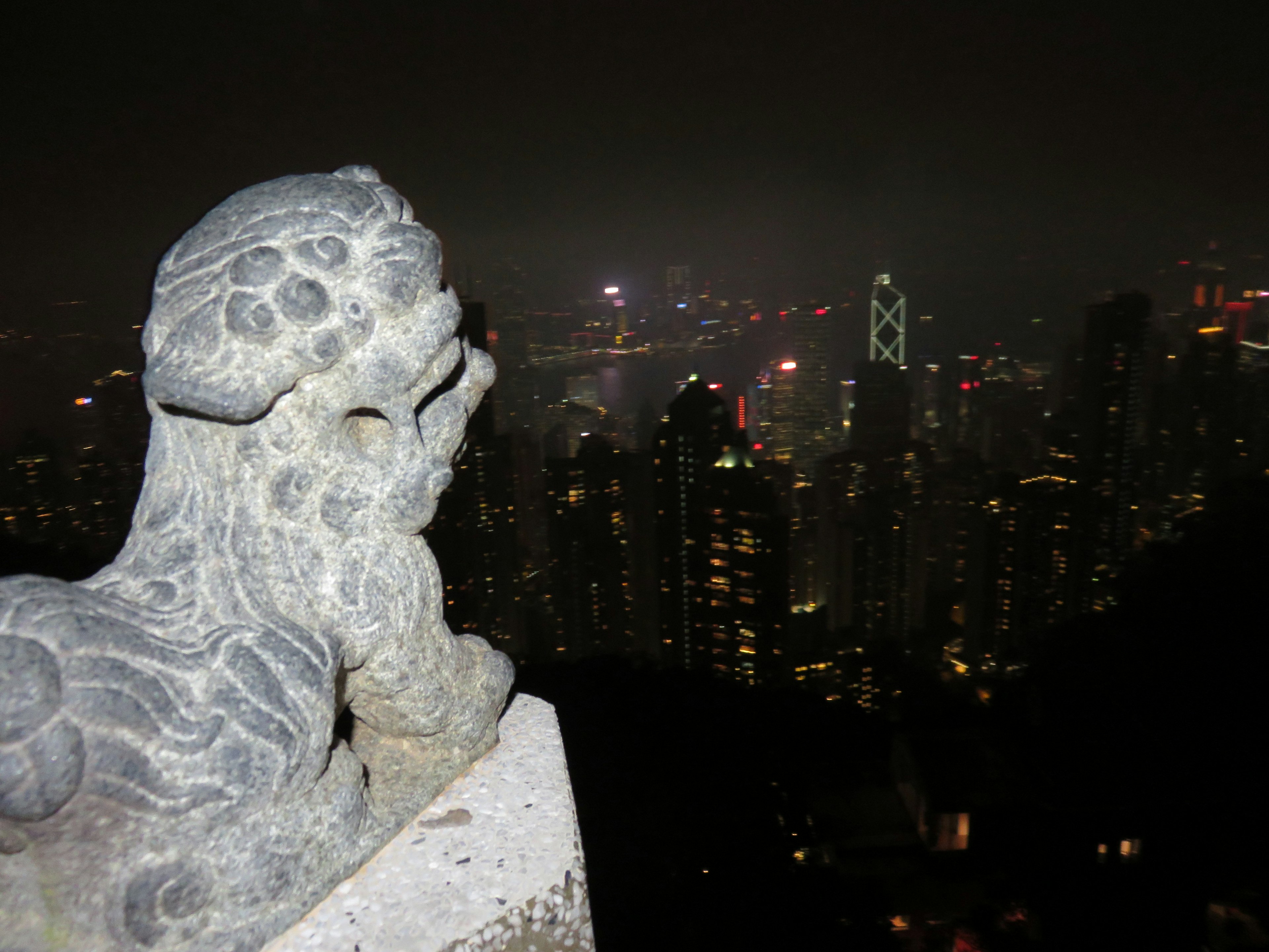 Stone lion statue overlooking the night view of Hong Kong skyline