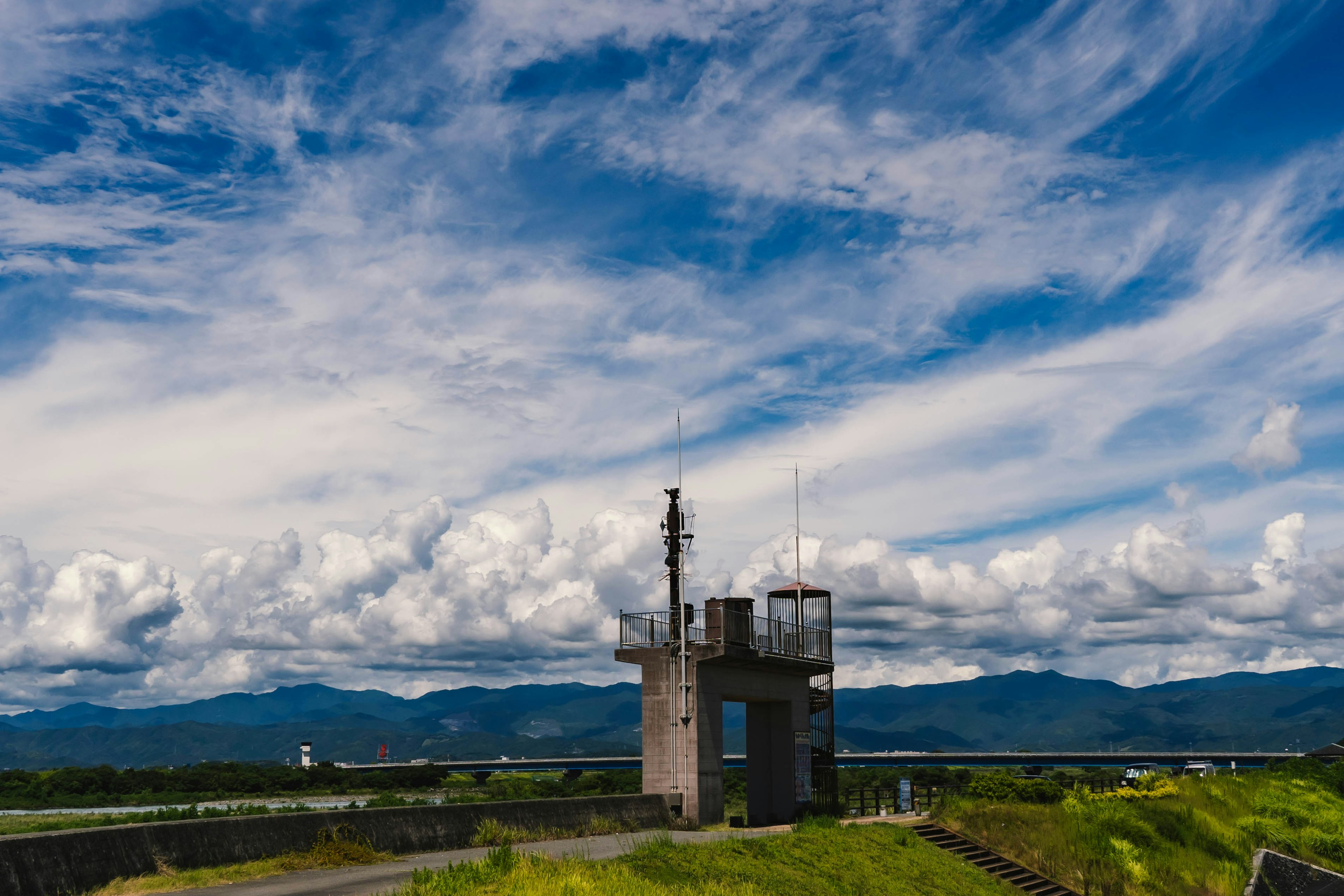 青空と雲が広がる風景に立つ小さな塔と緑の草地