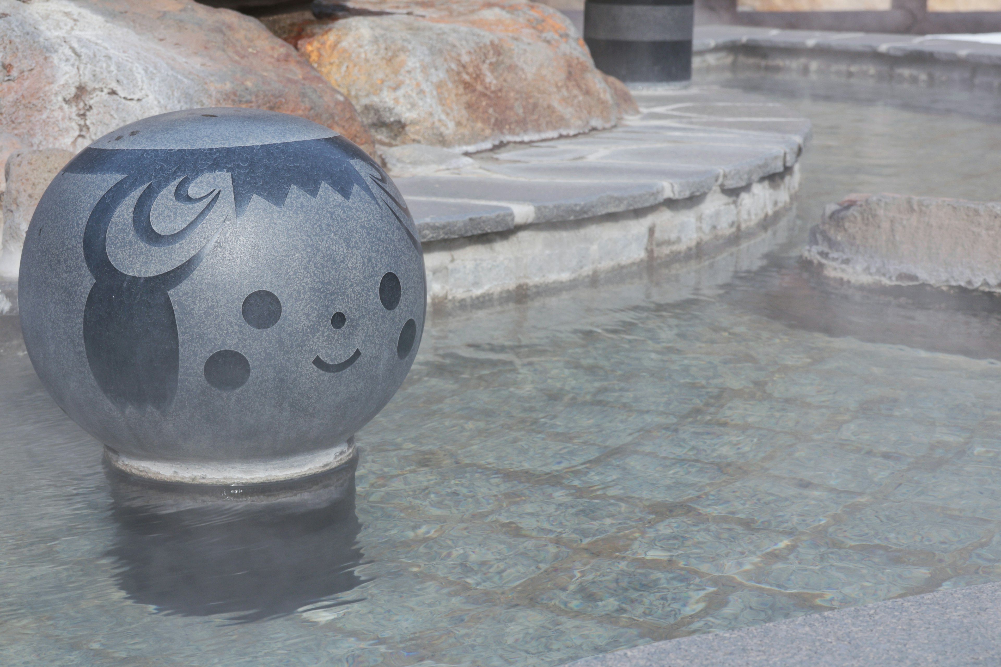 A cute stone ball with a smiling face floating in a hot spring