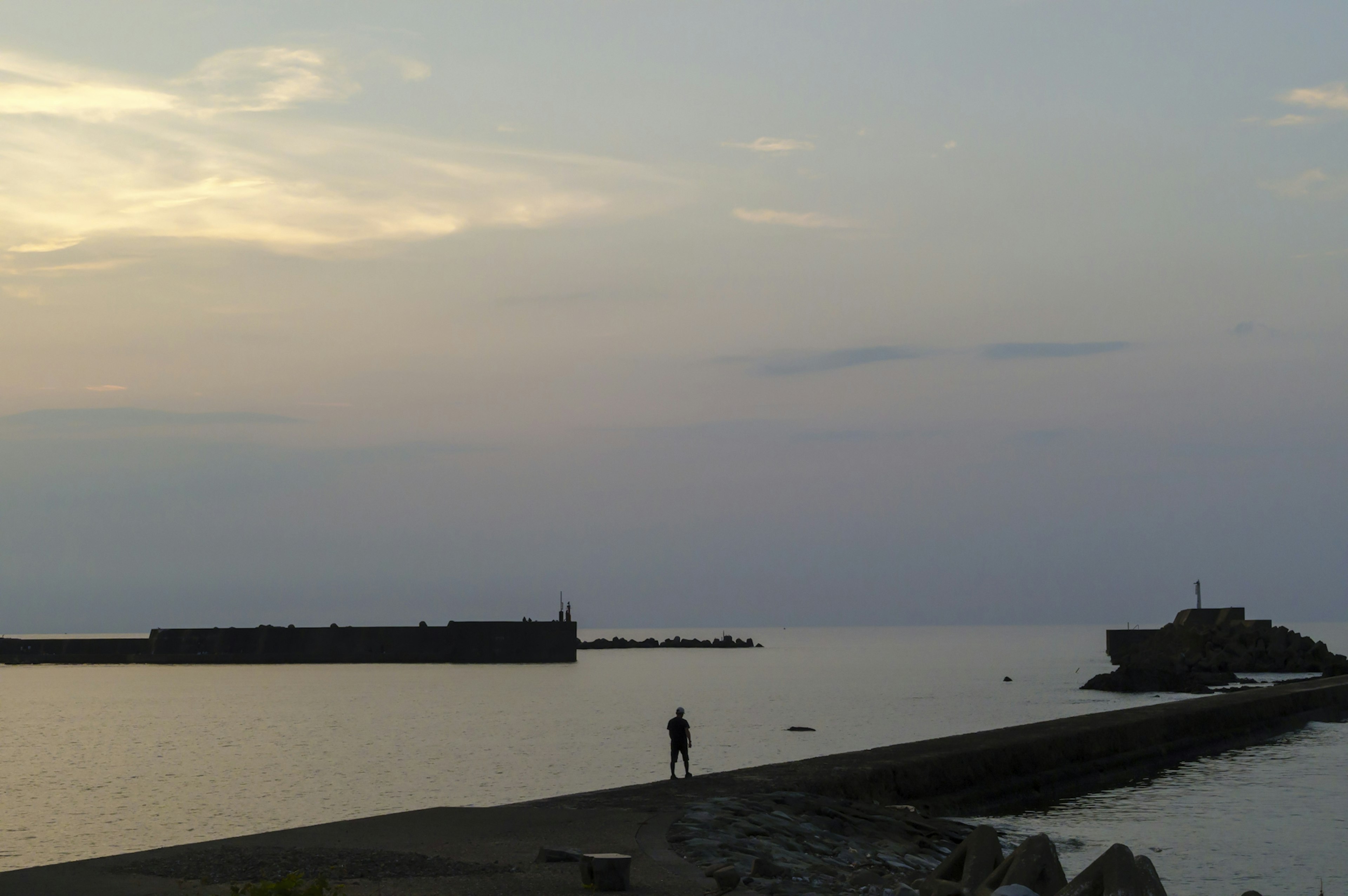 Silhouetted figure standing on a quiet coastline at sunset