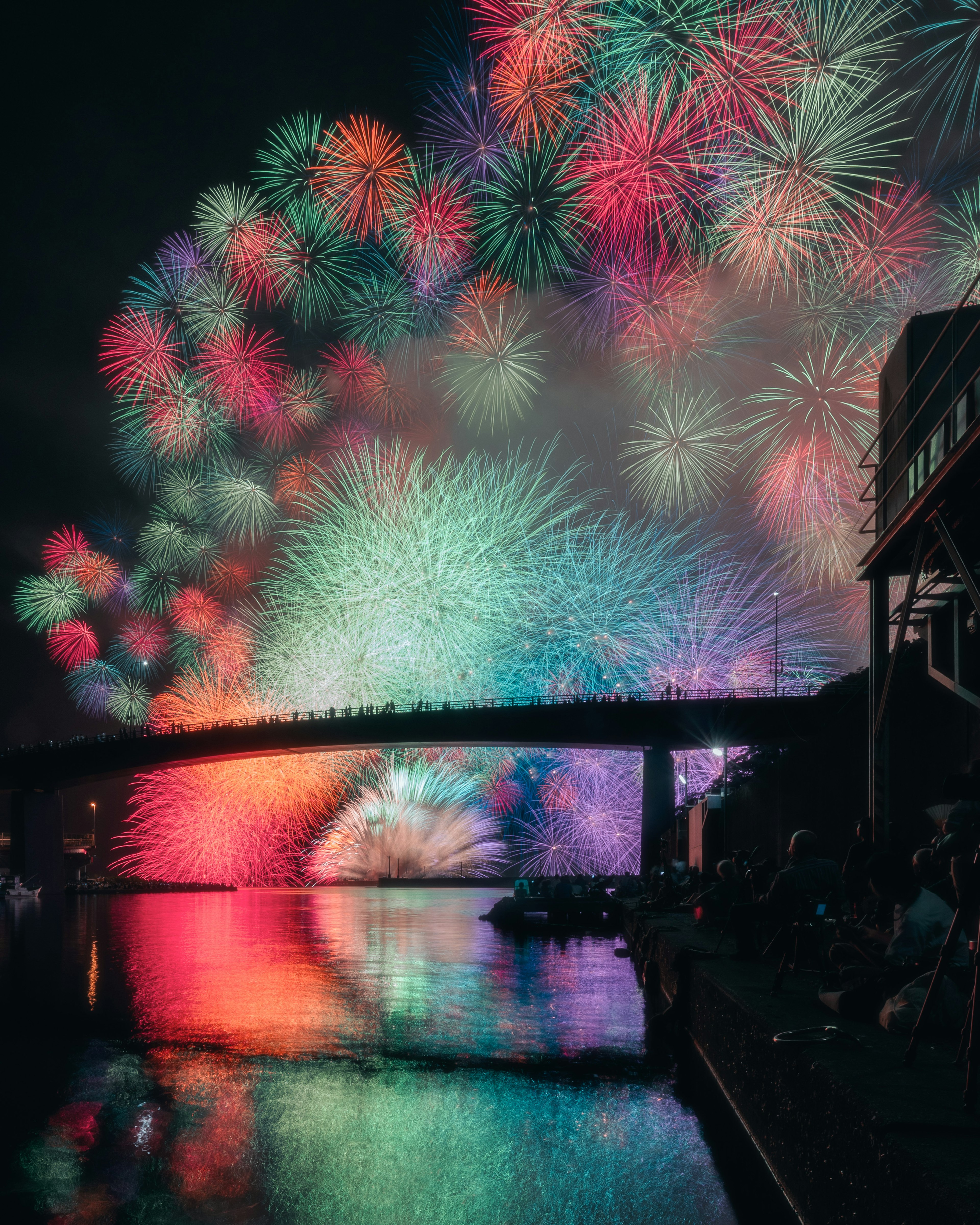 Fuochi d'artificio colorati illuminano il cielo notturno con un ponte e riflessi sull'acqua