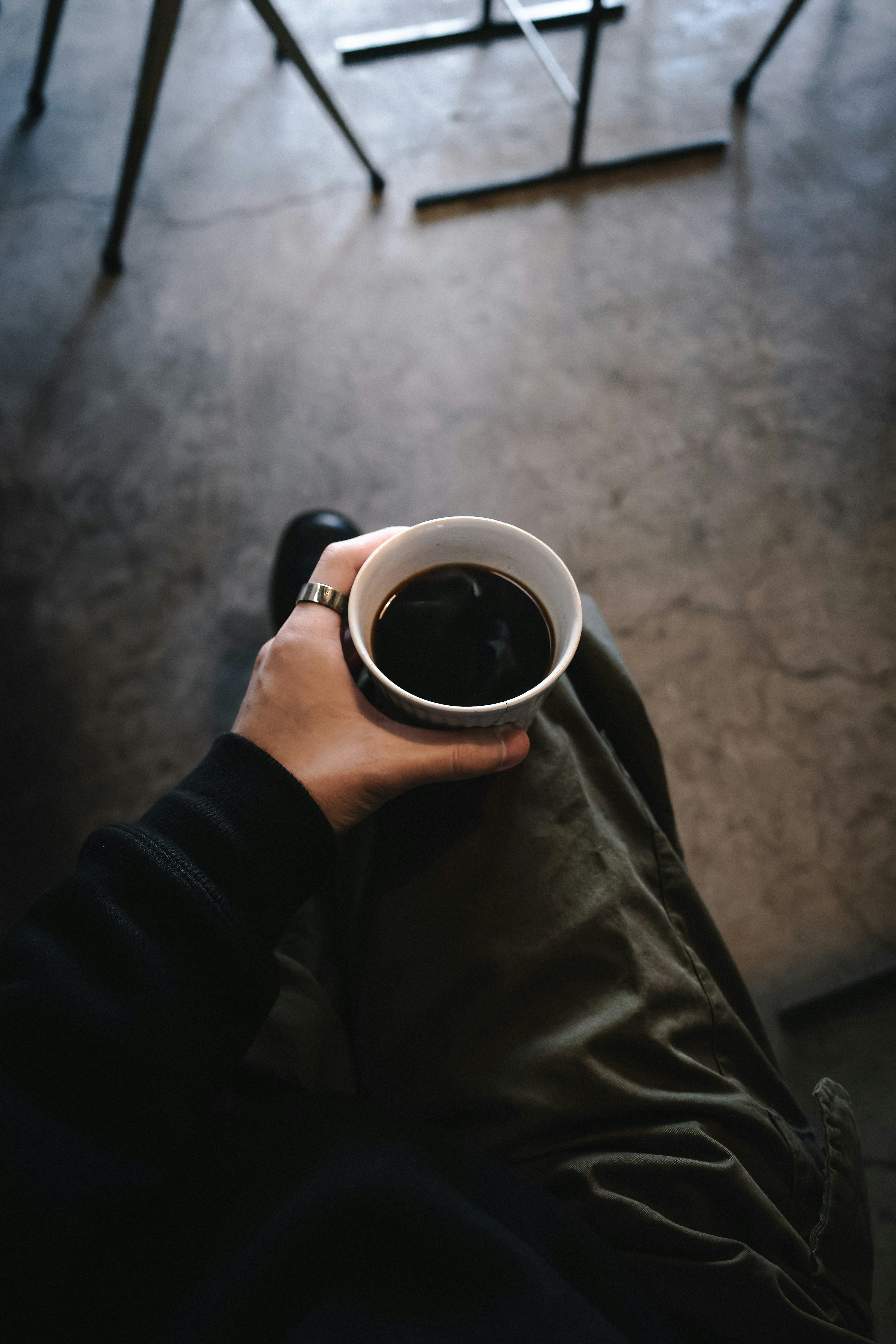 A hand holding a coffee cup with a person's legs crossed