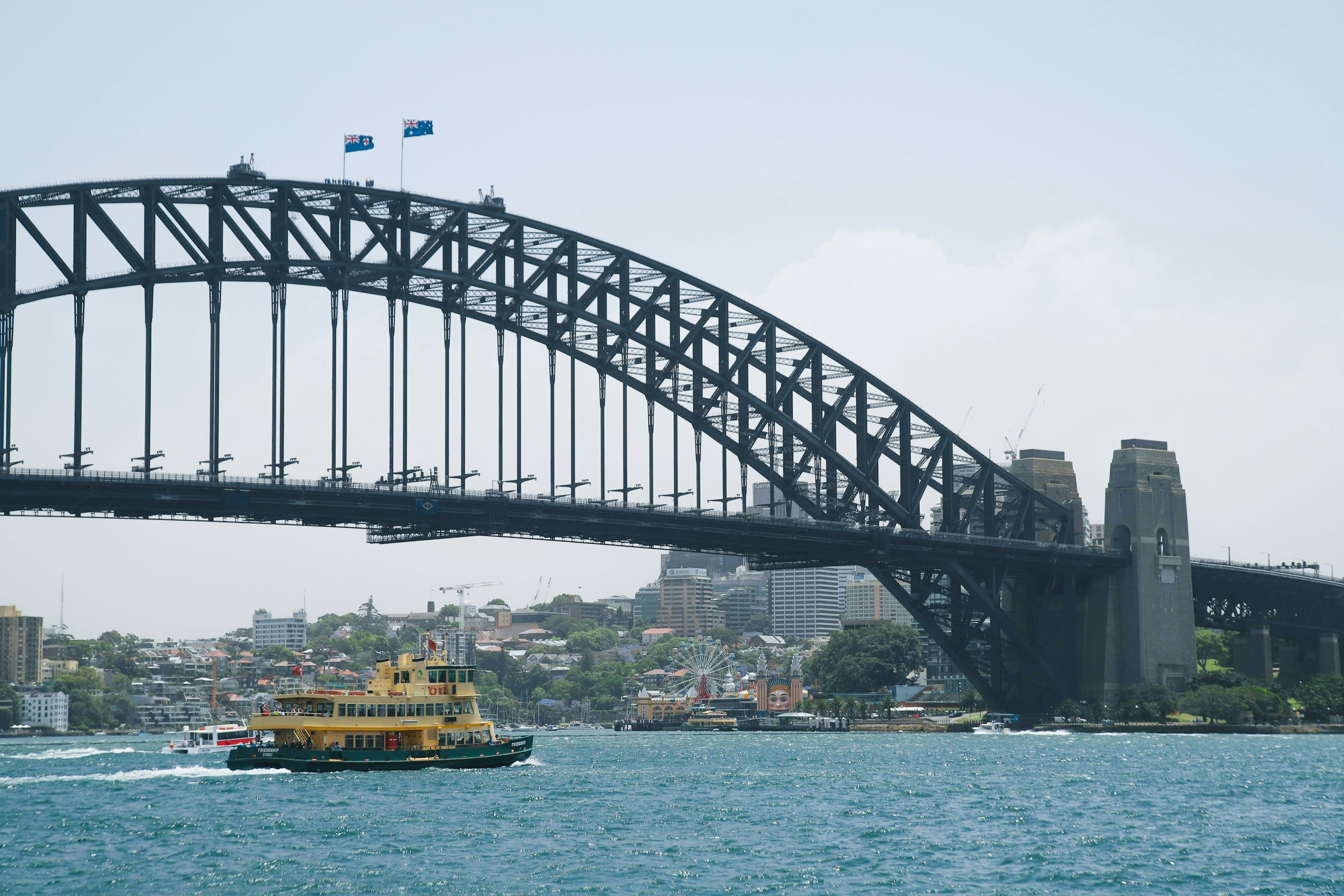 Ferry yang lewat di bawah Jembatan Pelabuhan Sydney dengan latar belakang kota