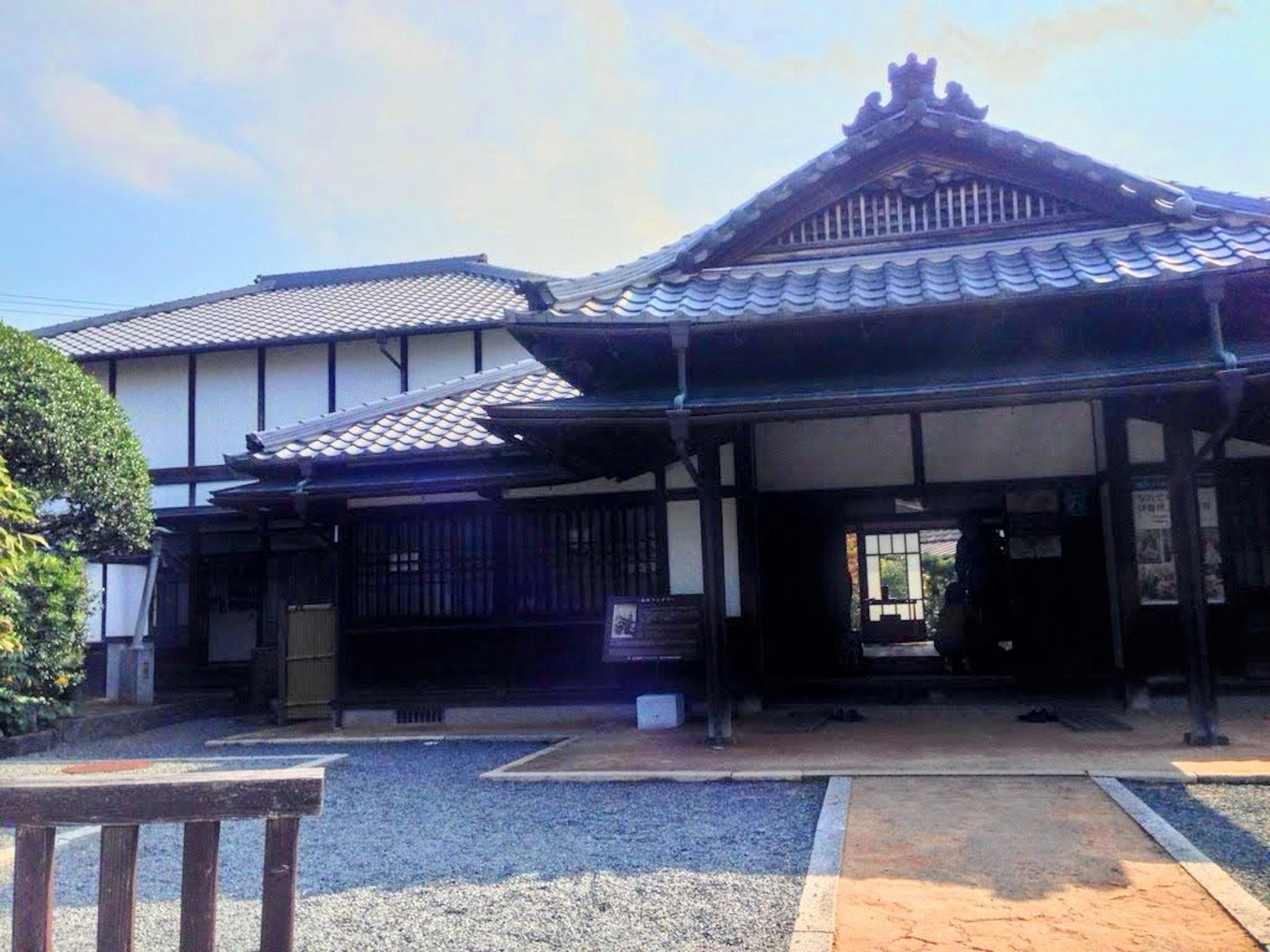 Bâtiment japonais traditionnel avec un toit en tuiles visible, présentant des chemins en pierre et de la verdure dans le jardin