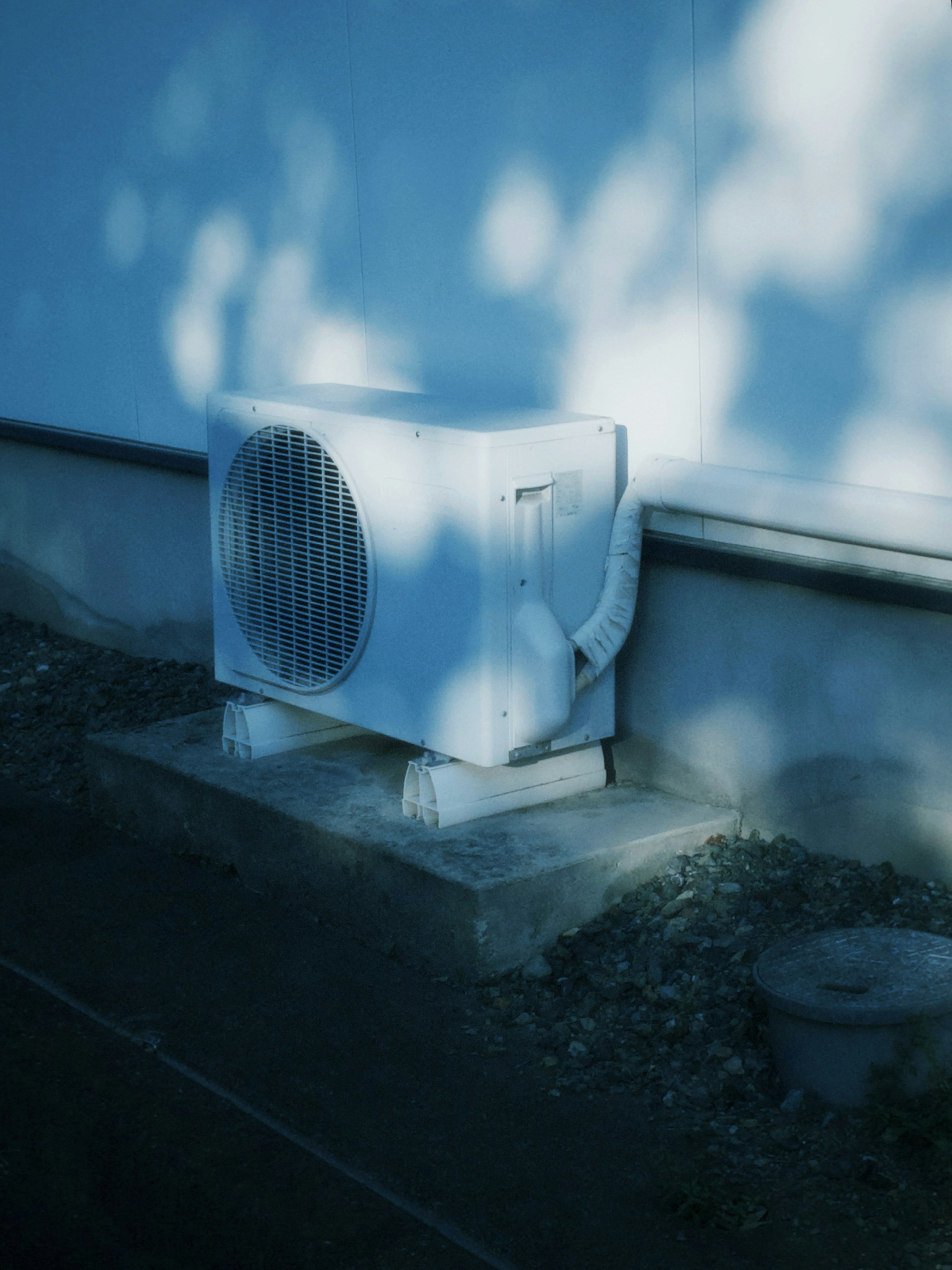 A white outdoor air conditioning unit positioned beside a wall