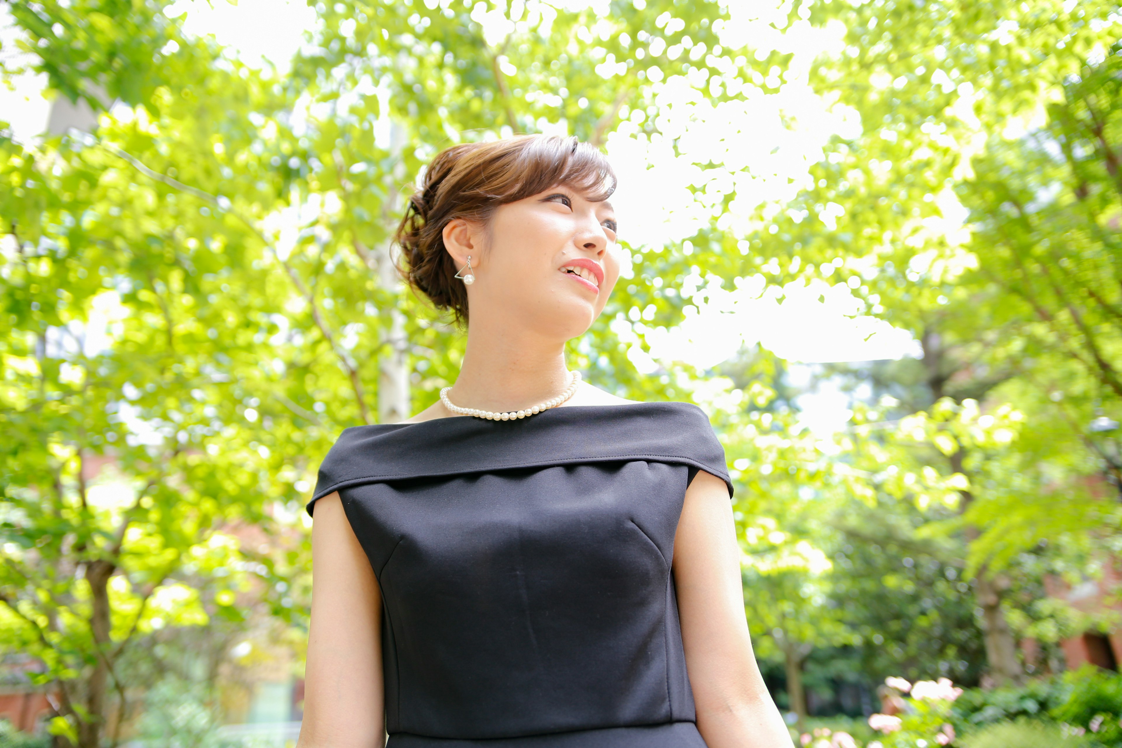 Une femme en robe noire souriant parmi des arbres verts