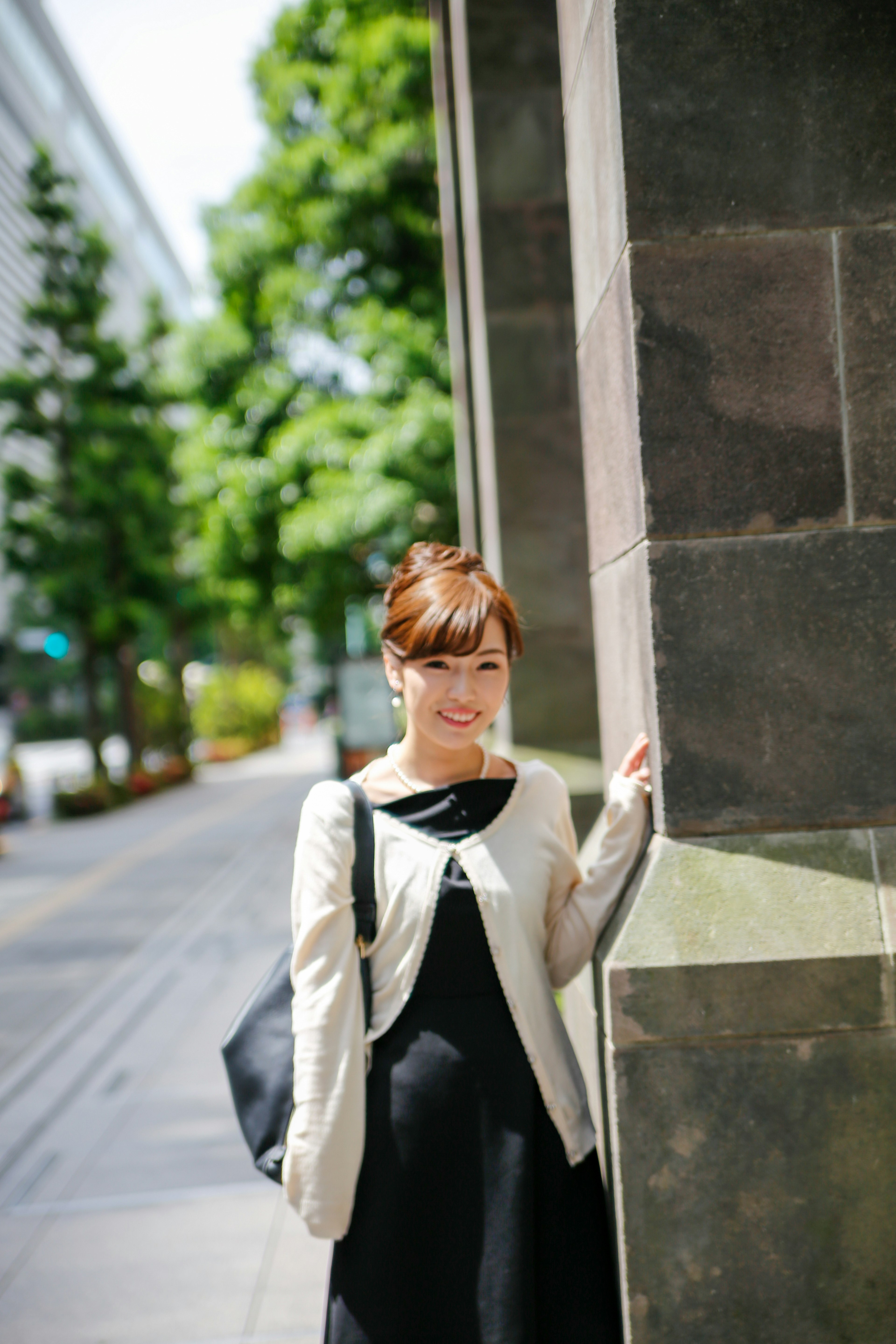 A woman standing at a street corner smiling at the camera wearing casual attire