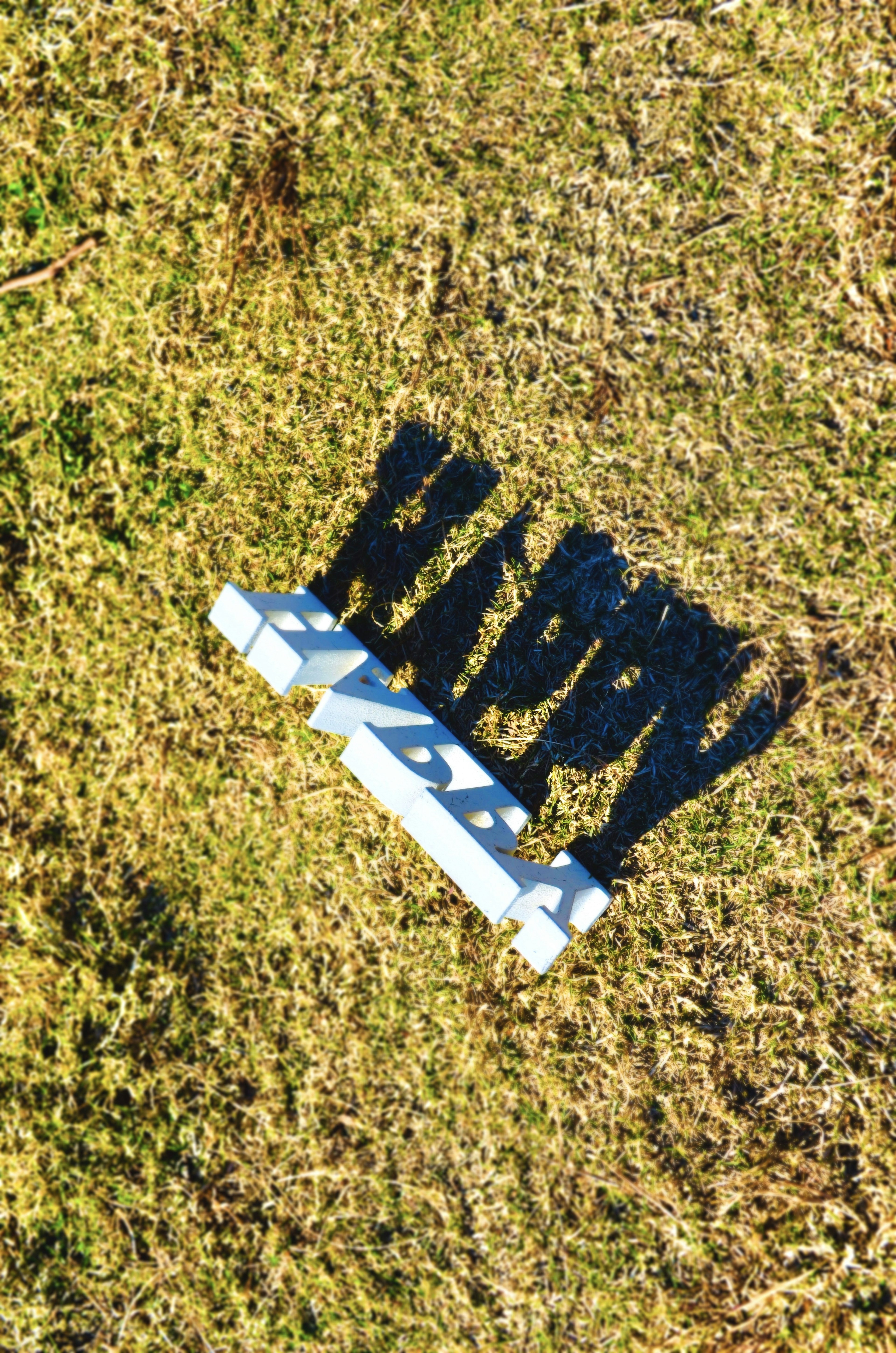 White letters spelling 'HAPPY' casting a shadow on grass