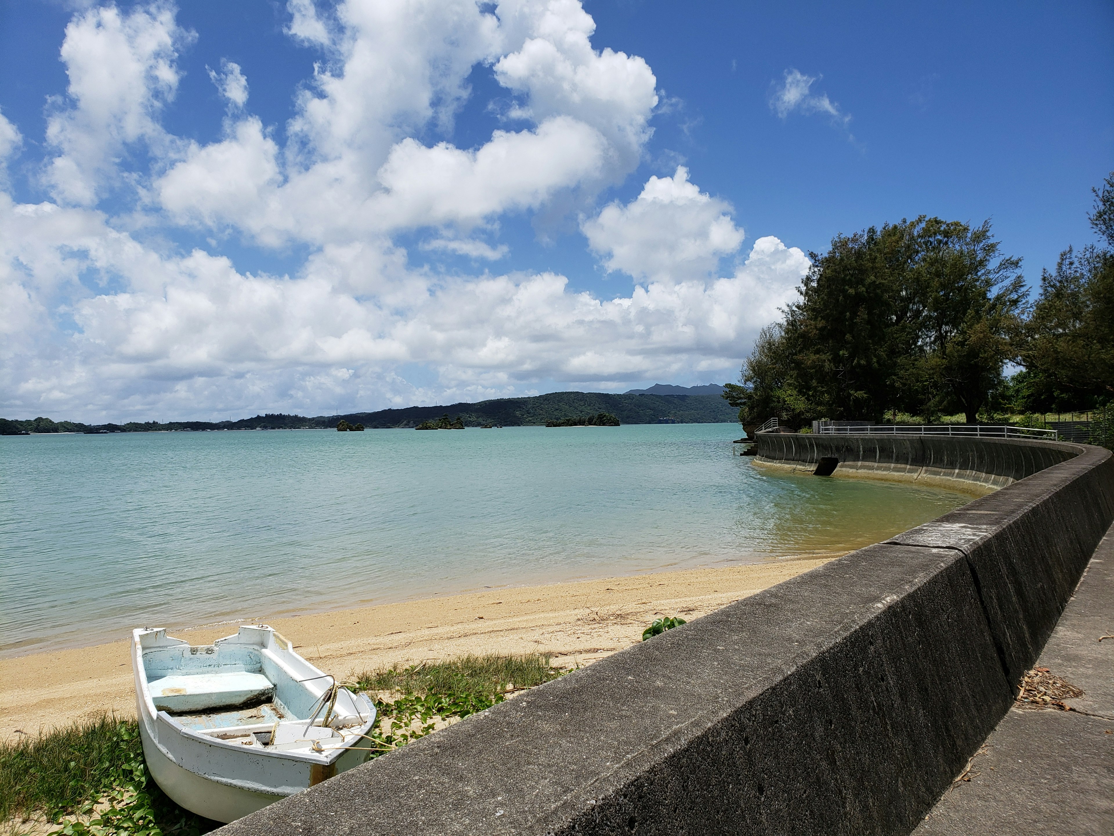 風景如畫的海灘景色 藍色海洋和白色雲朵 海岸上的小船和石堤