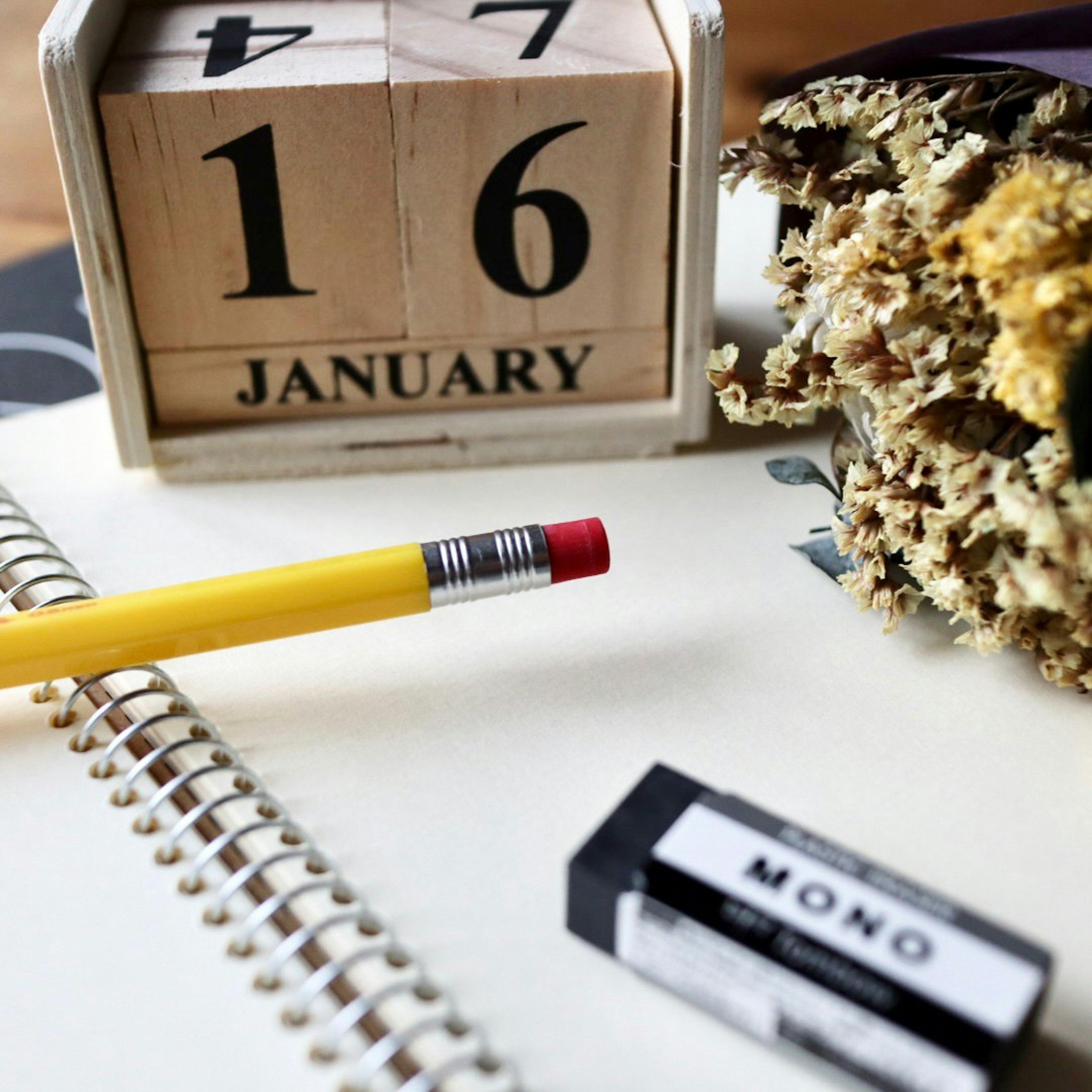 Wooden calendar displaying January 16 with a yellow pencil and eraser on a notebook