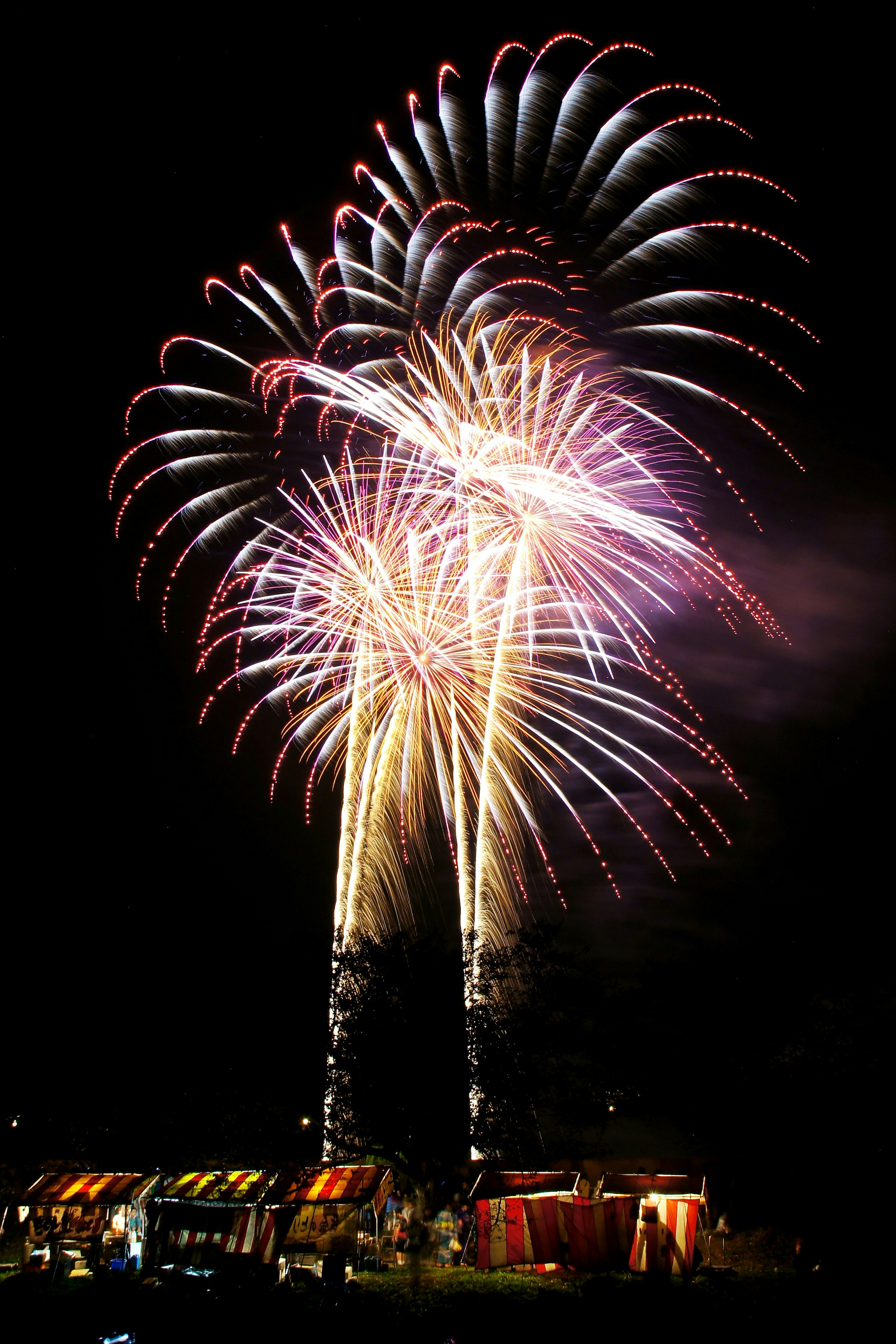 Vibrant fireworks exploding in the night sky with colorful stalls below