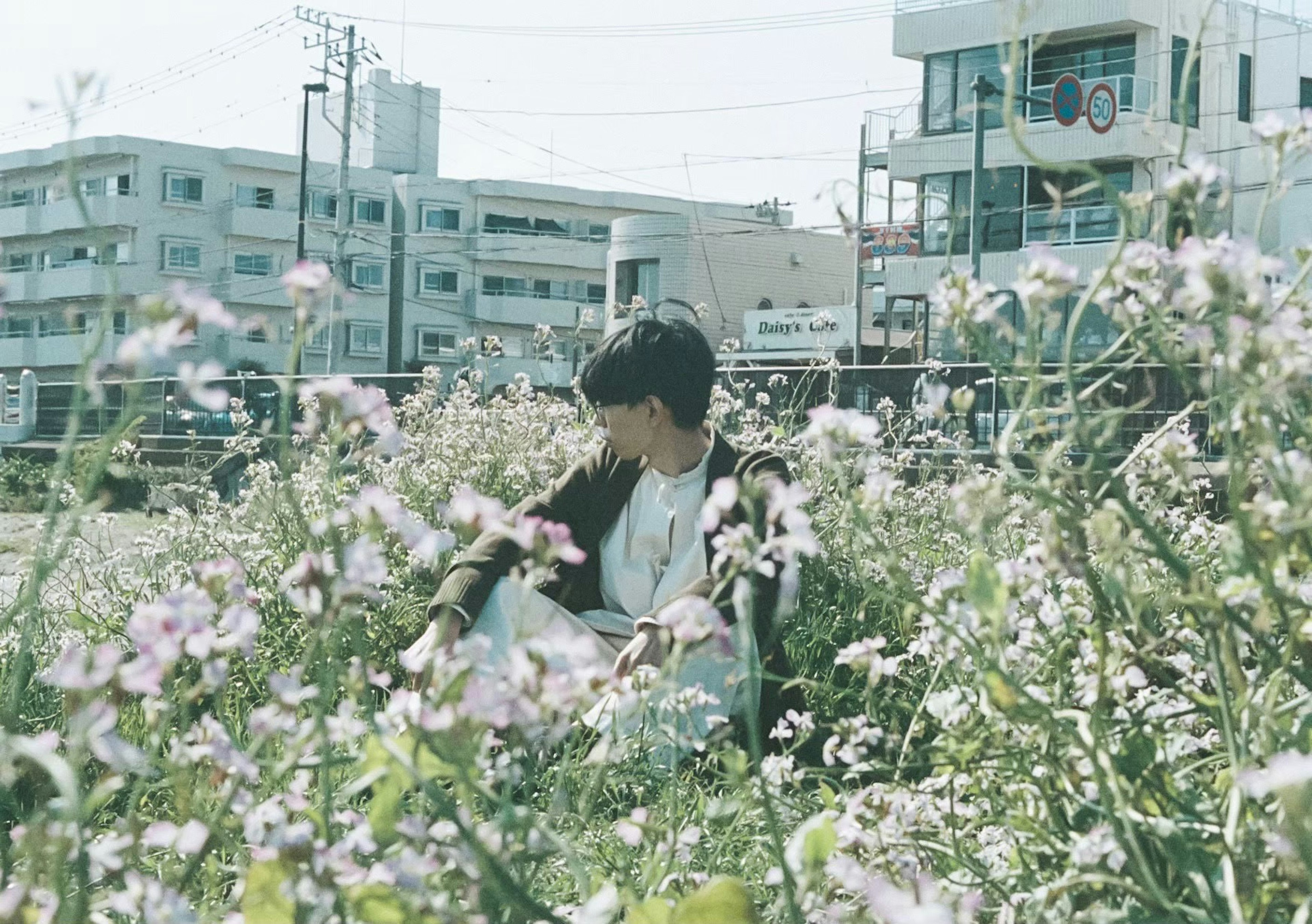 A young person sitting among blooming flowers in an urban setting