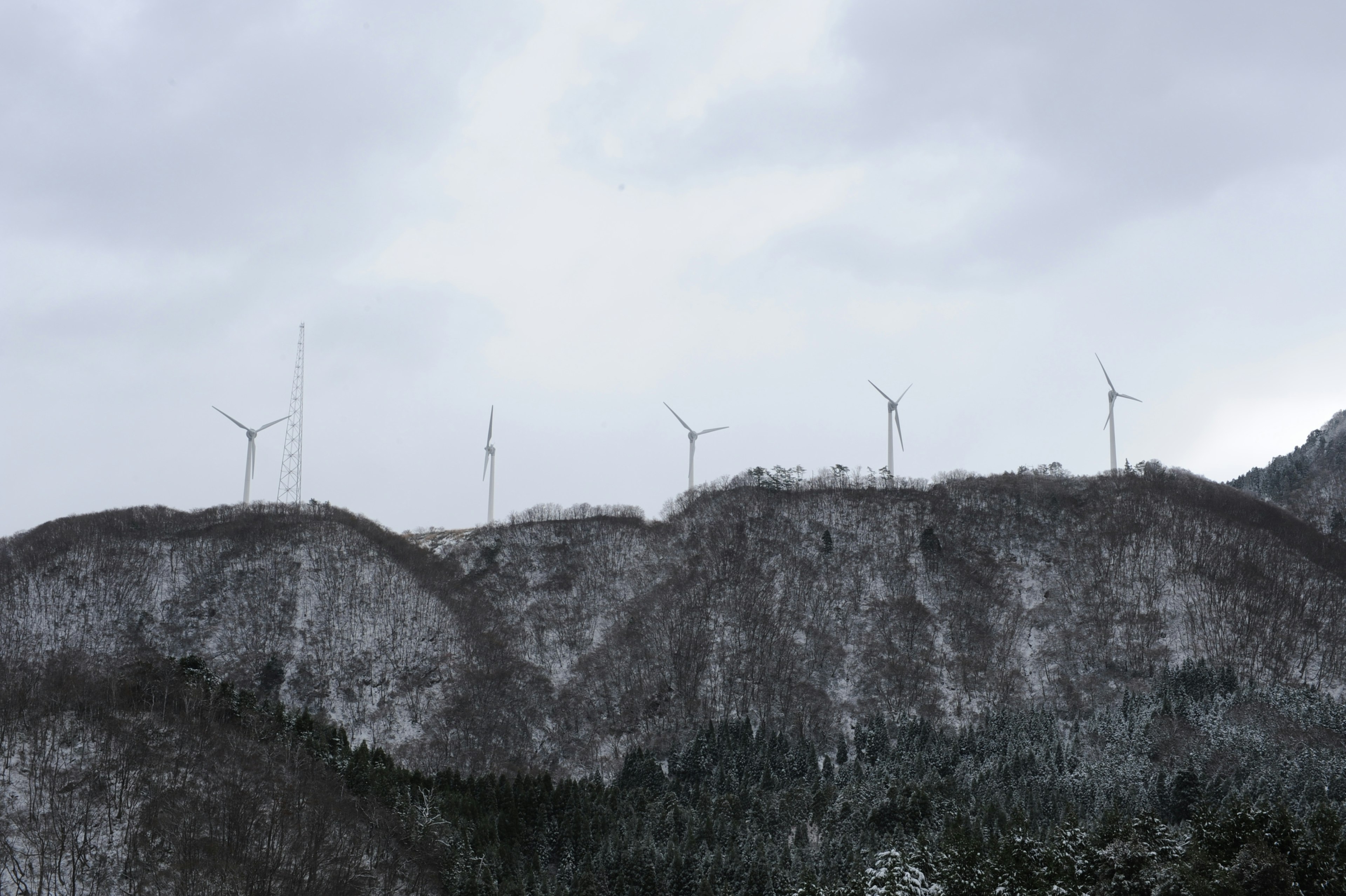 雪覆蓋的山上風力發電機在多雲的天空下