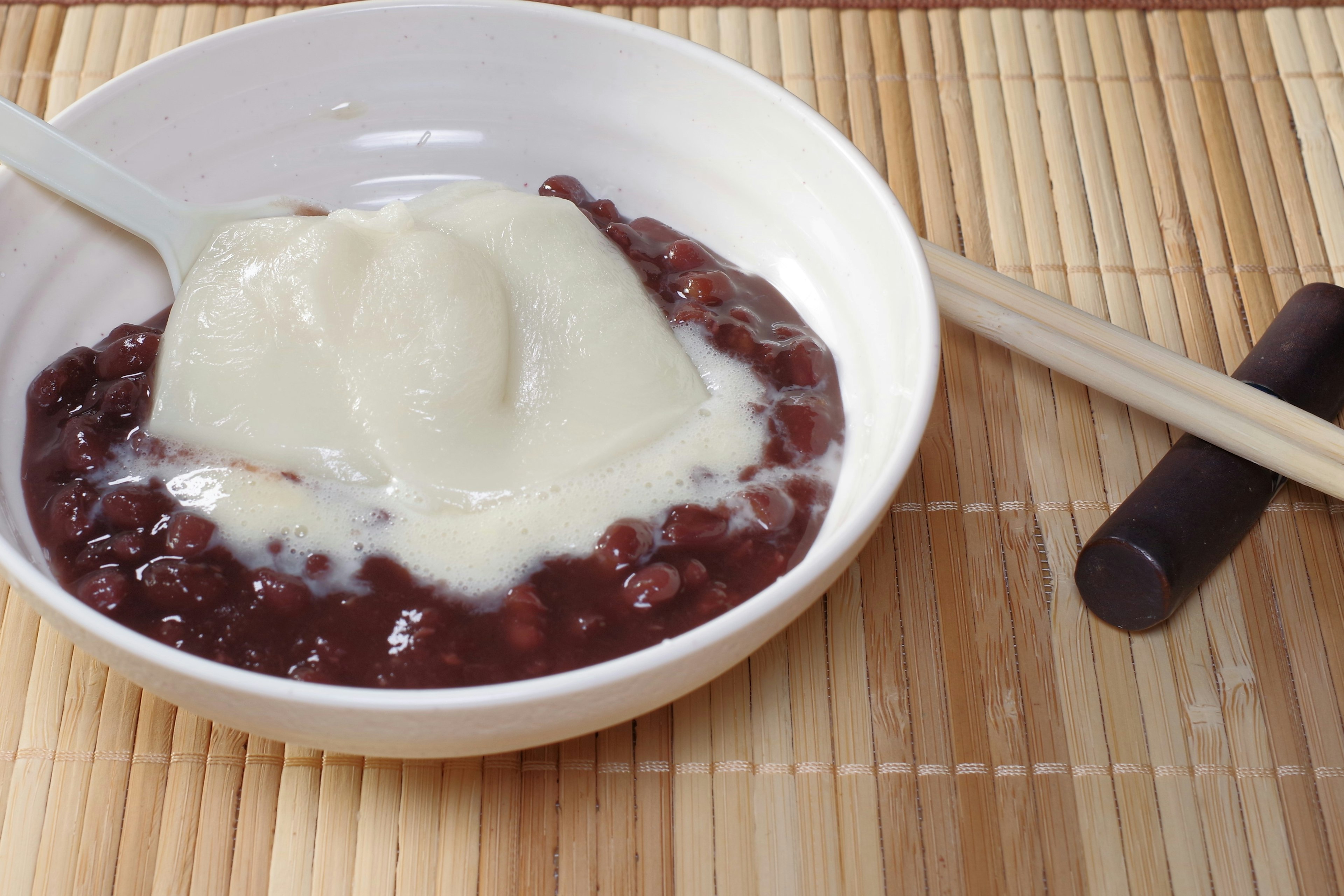 Una ciotola di pasta di fagioli rossi guarnita con gelato alla vaniglia servita con bacchette