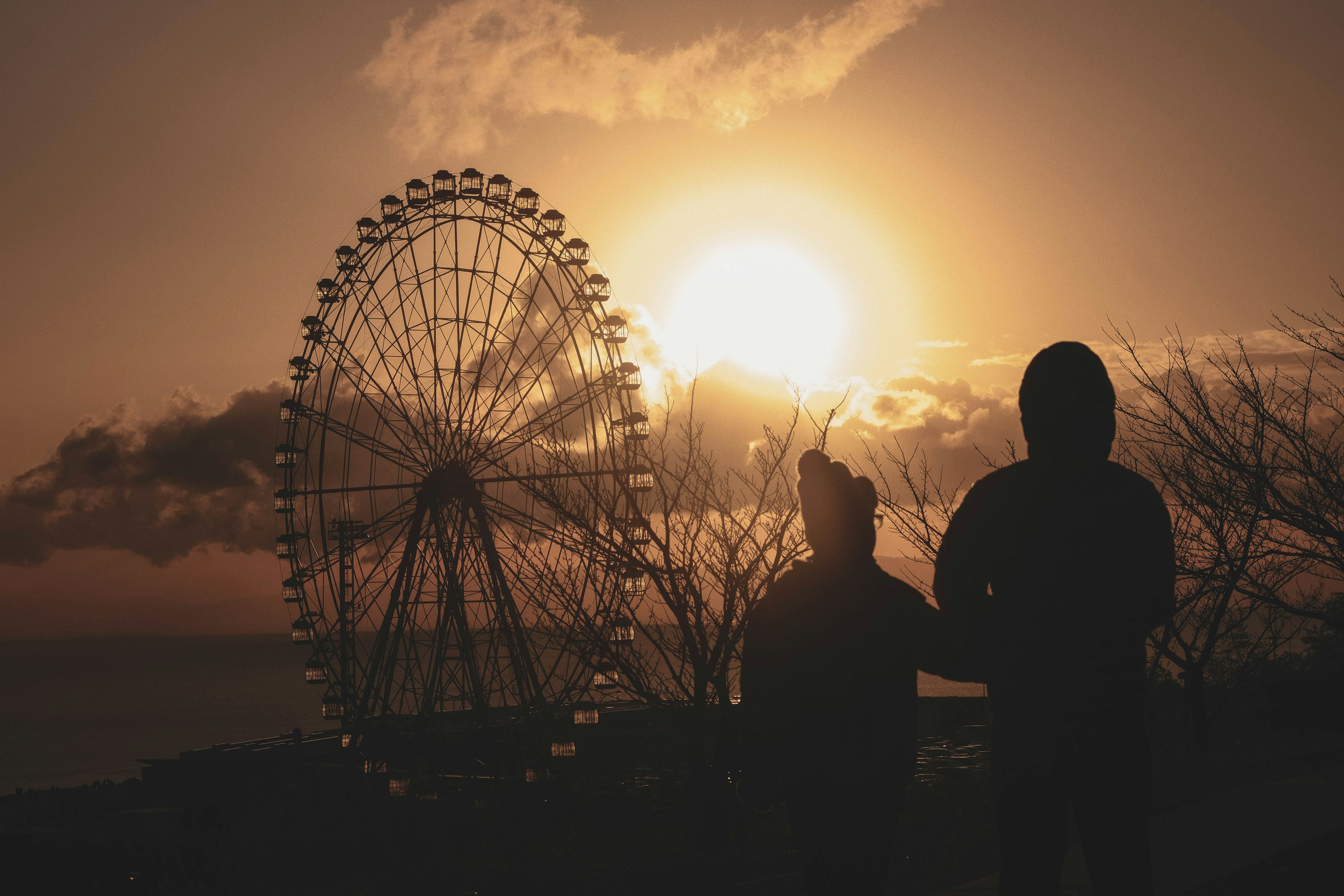 Siluet pasangan dengan roda ferris di latar belakang matahari terbenam