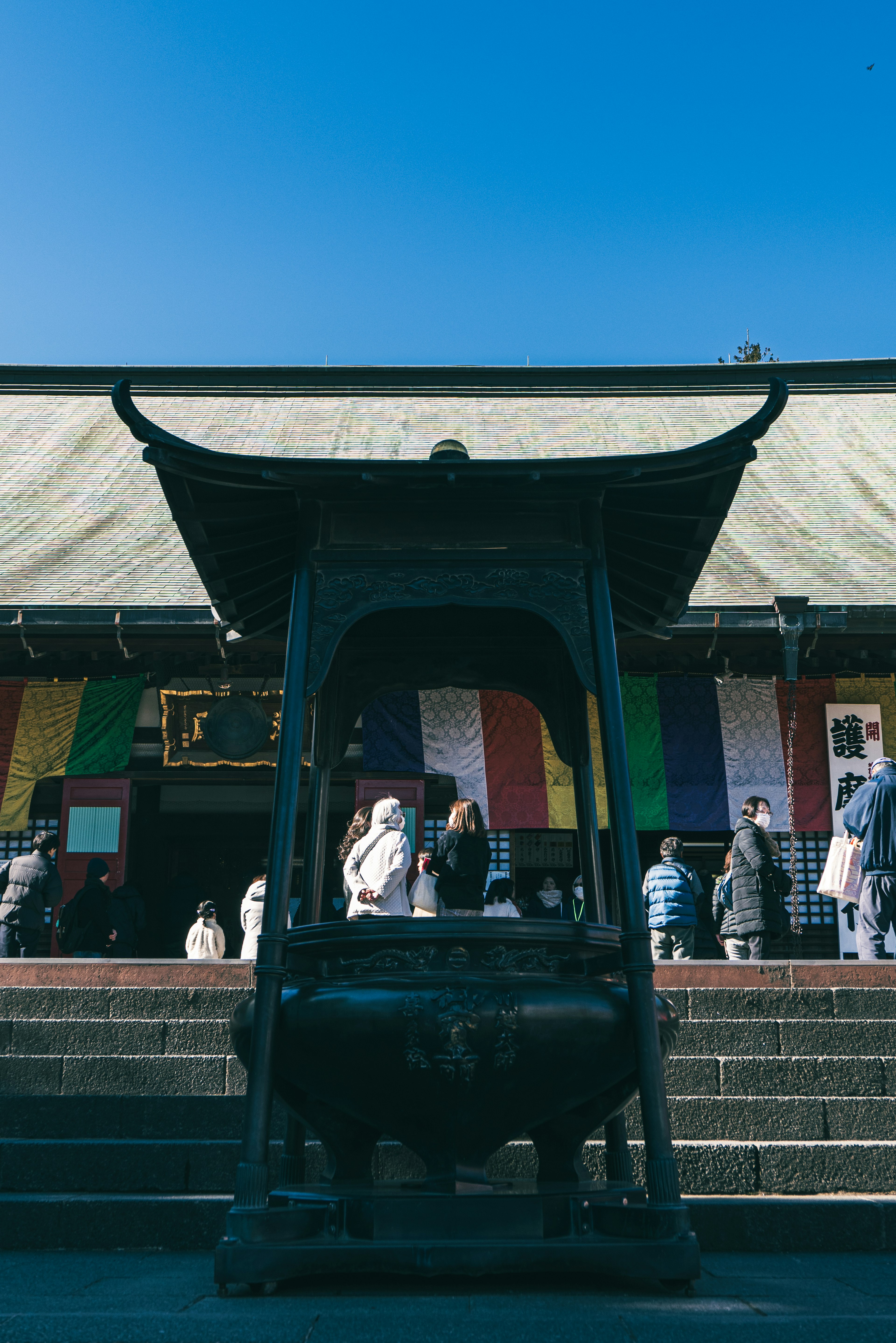 青空の下で人々が集まる寺院の前にある大きな香炉