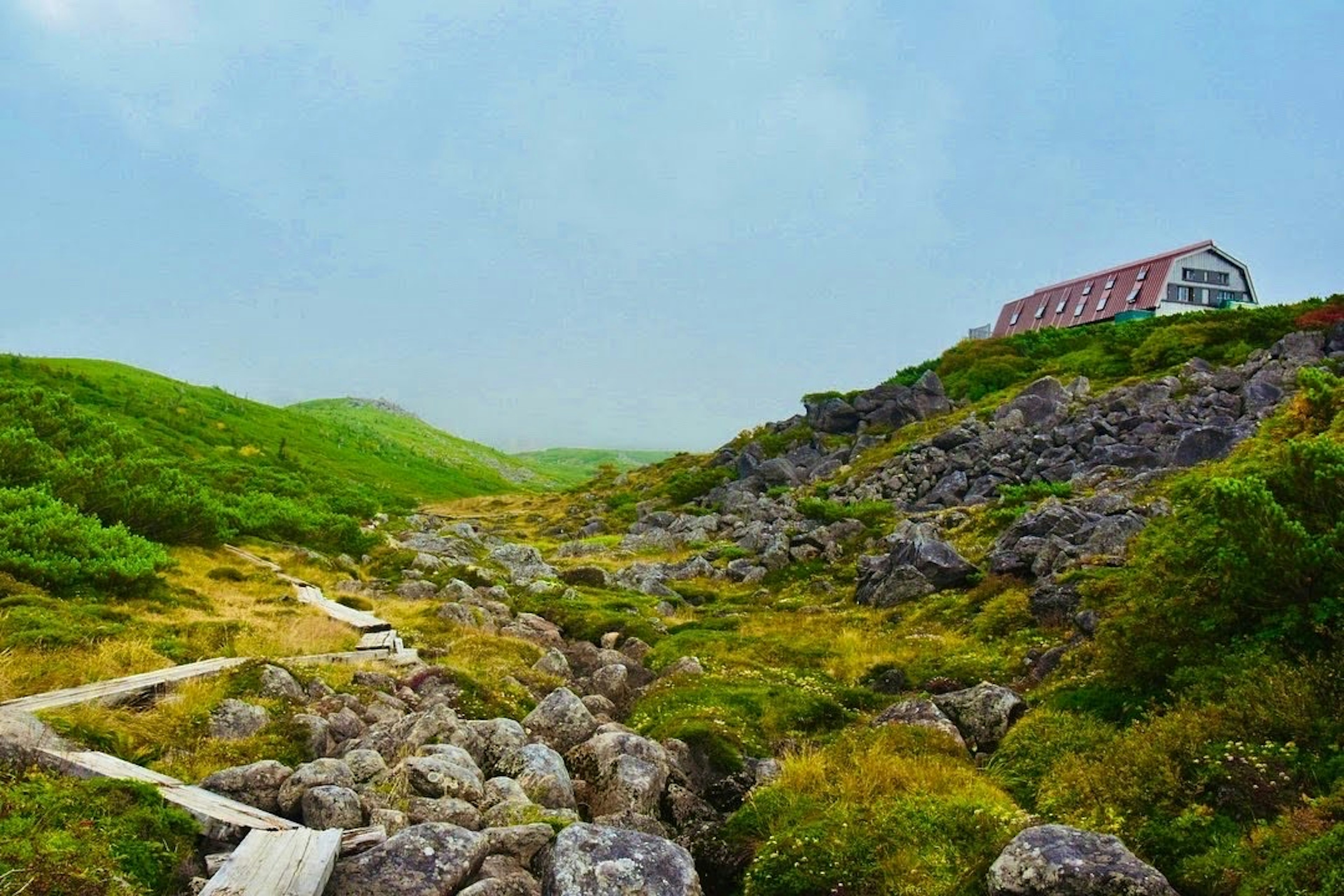 Vista panoramica di una casa con tetto rosso tra colline verdi e terreno roccioso