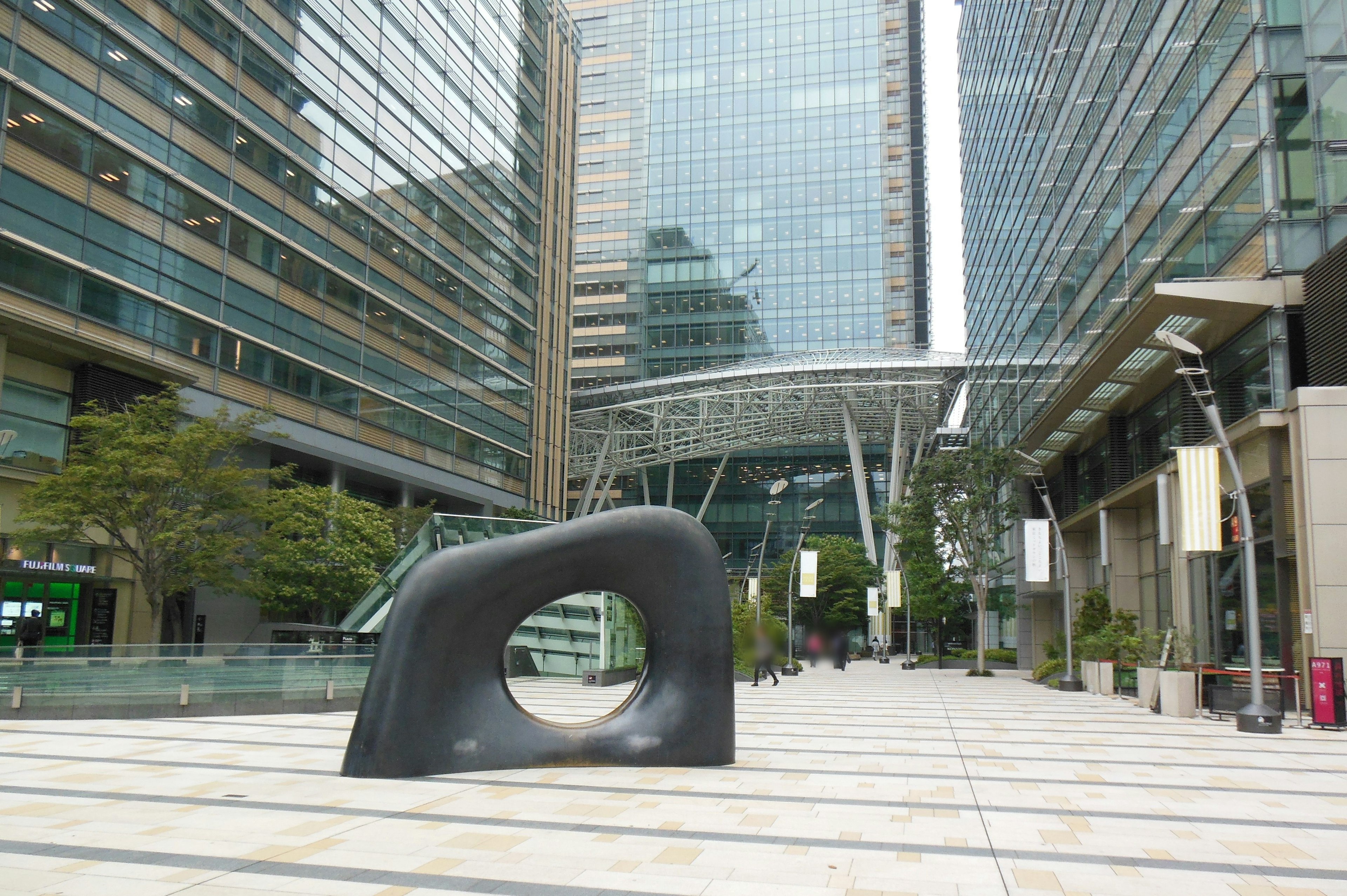 Black sculpture in a paved plaza surrounded by modern buildings