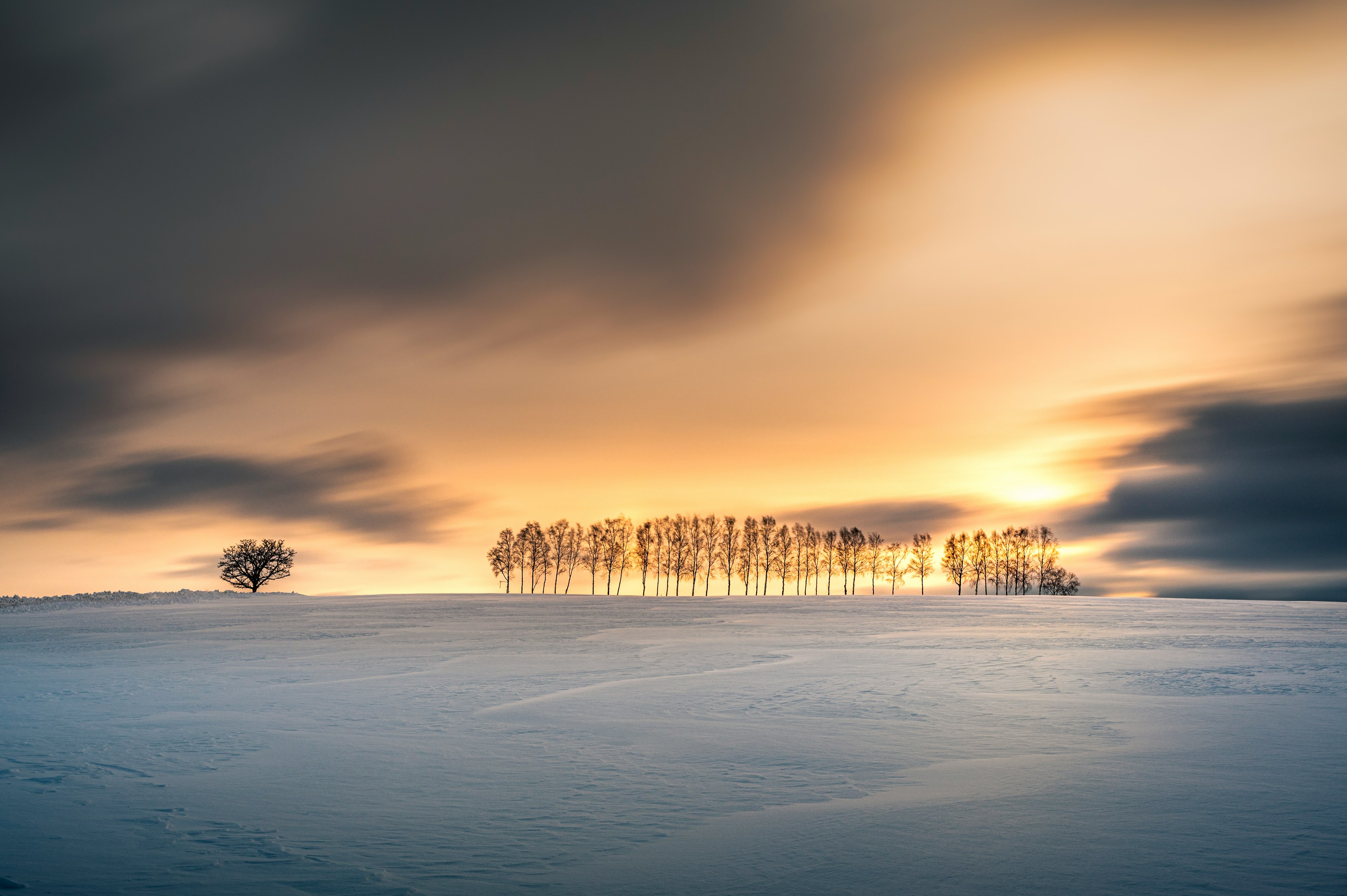 Paisaje invernal con un campo nevado y un cielo de atardecer naranja