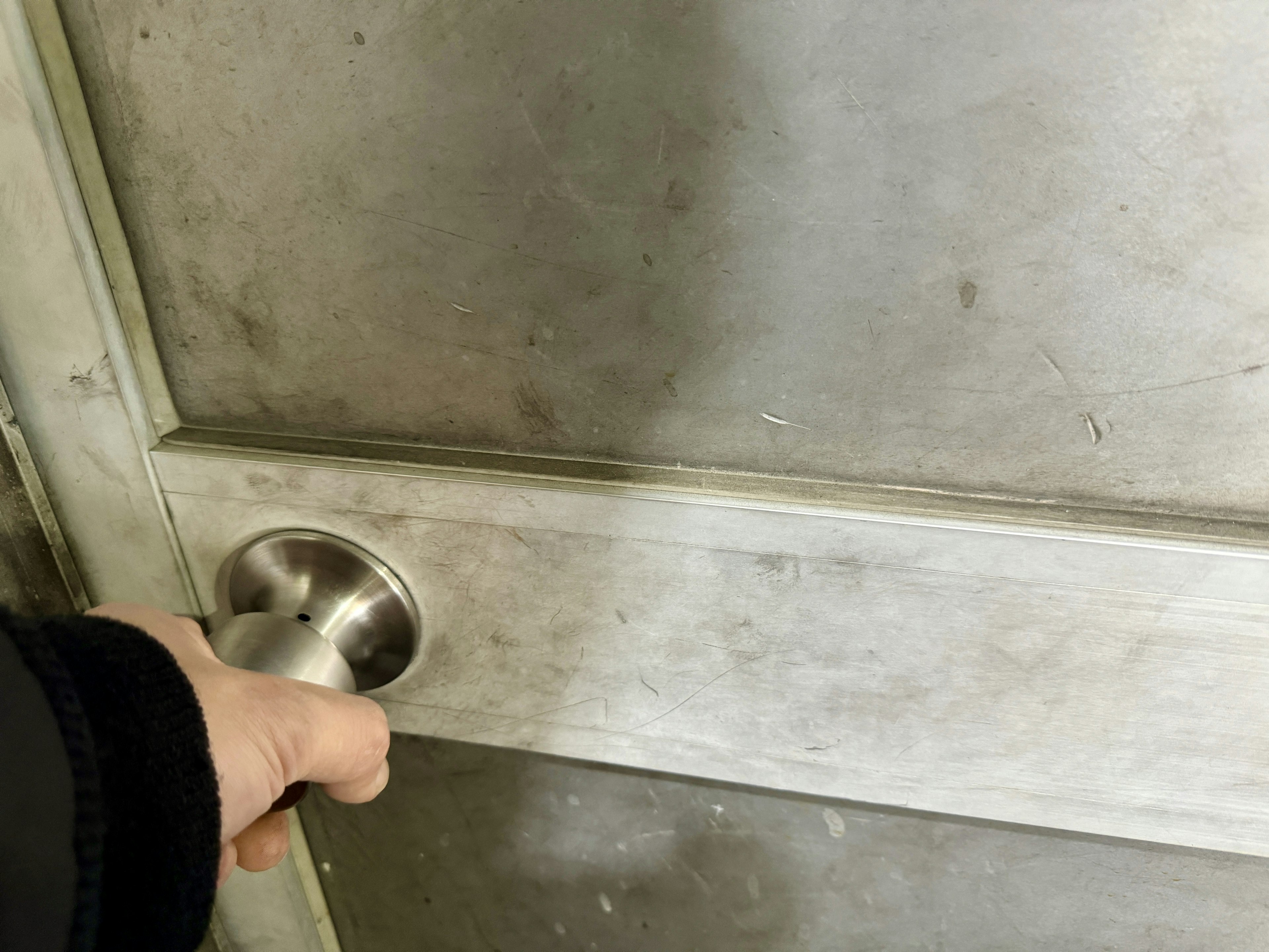 Close-up of a hand gripping a silver door knob on a metallic door