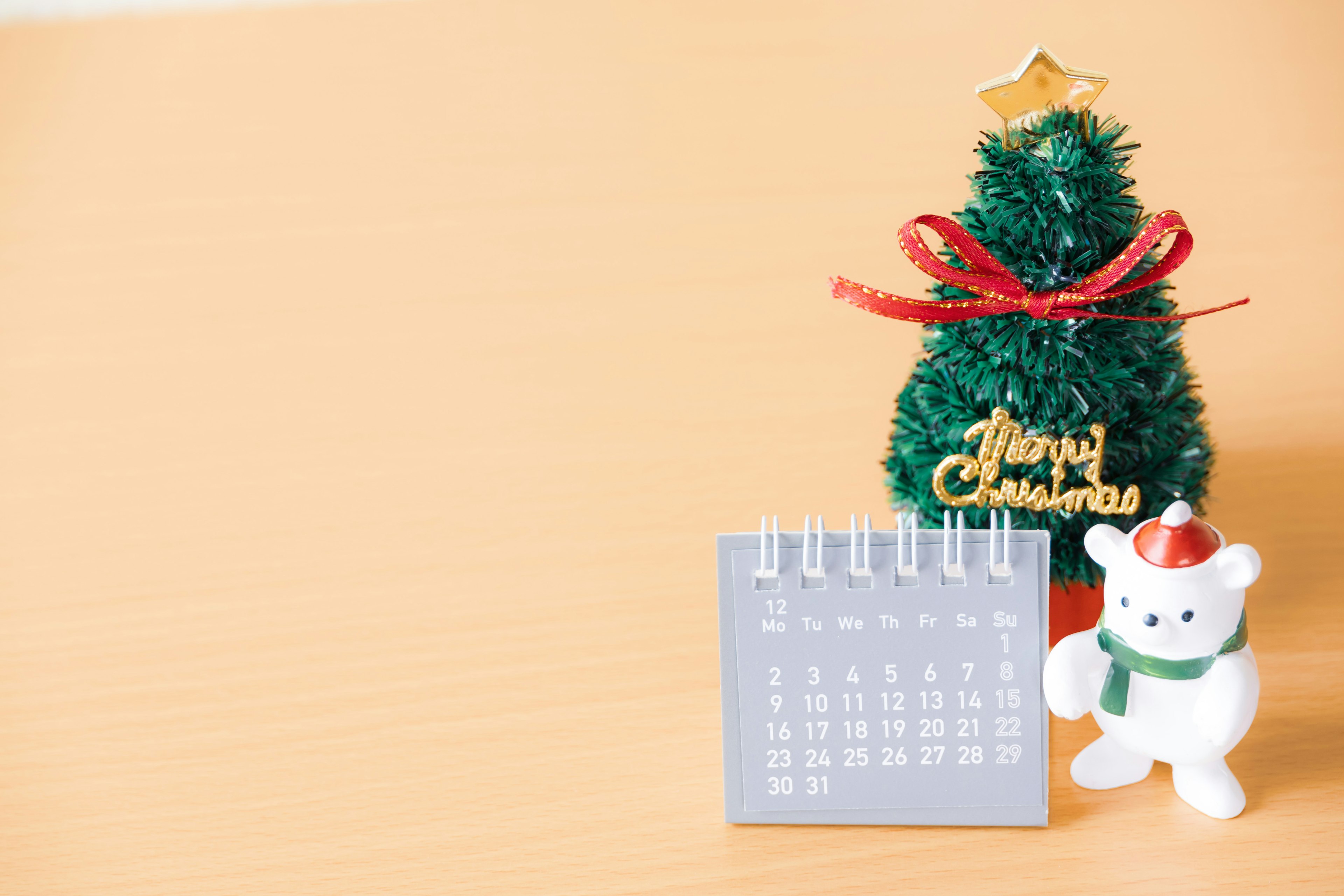 A Christmas-themed image featuring a green tree with a star and ribbon alongside a calendar and a white bear figurine