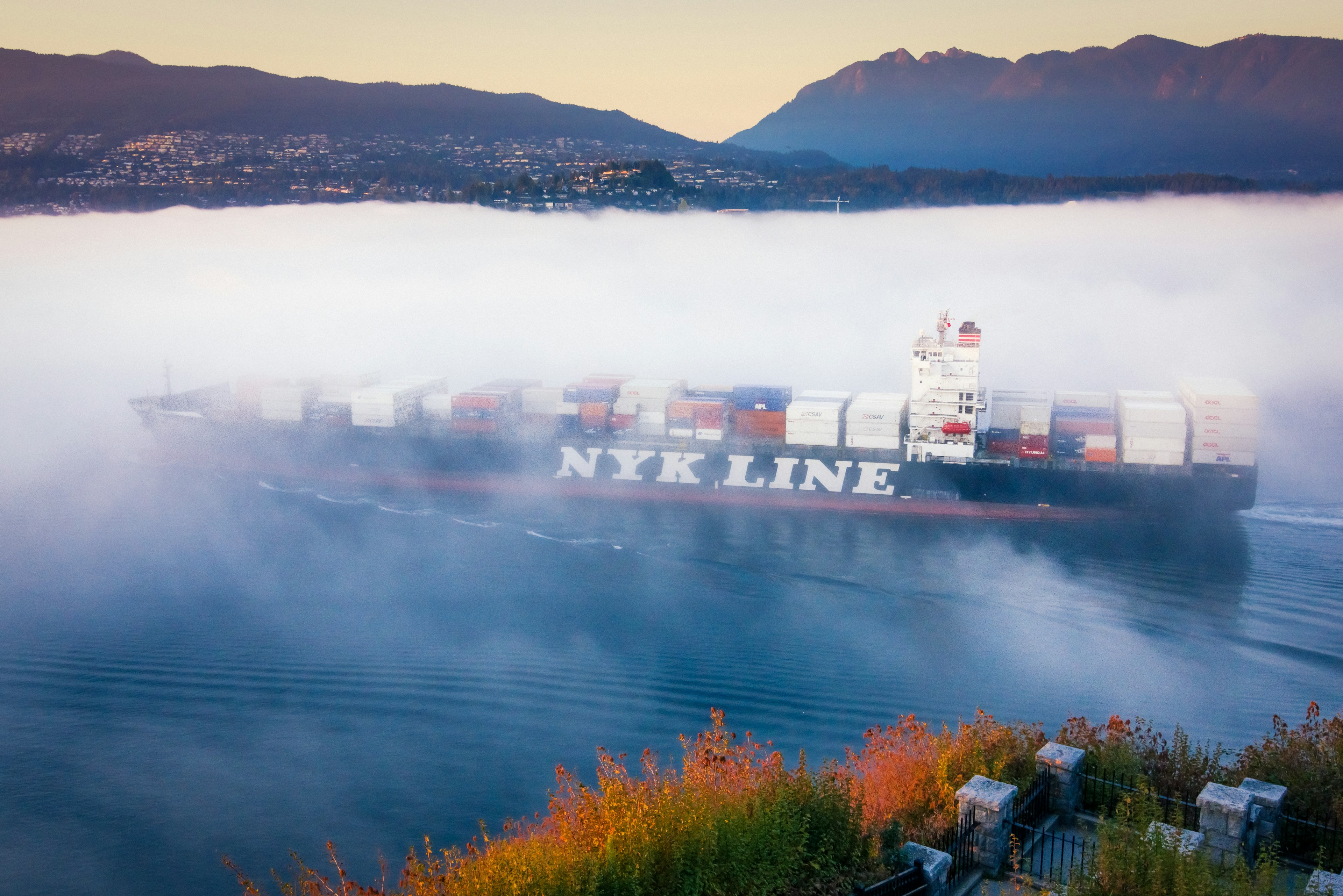 Containerschiff NTK Line, das durch Nebel mit Bergen im Hintergrund fährt