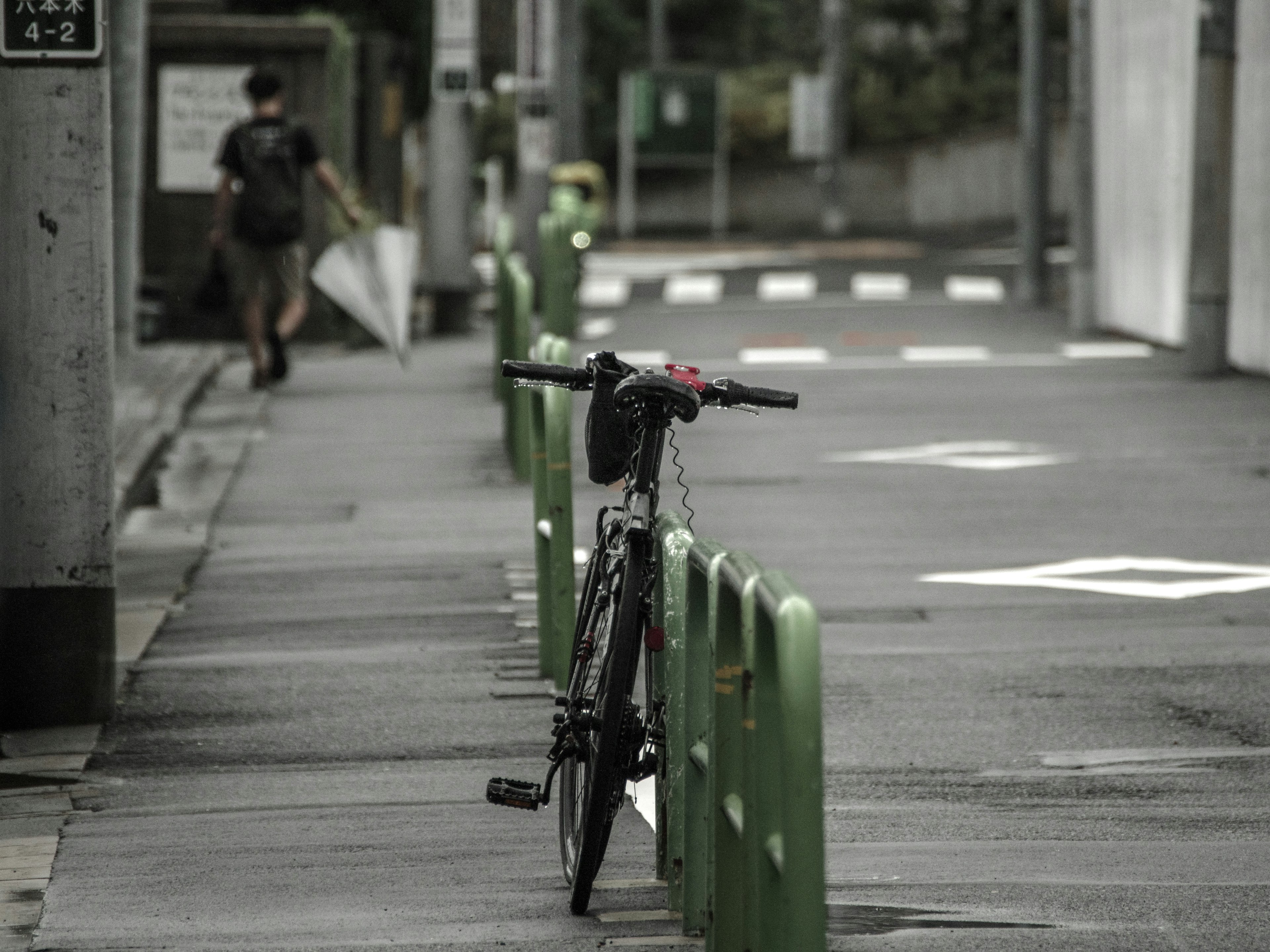 A bicycle leaning against a green barrier with a distant pedestrian