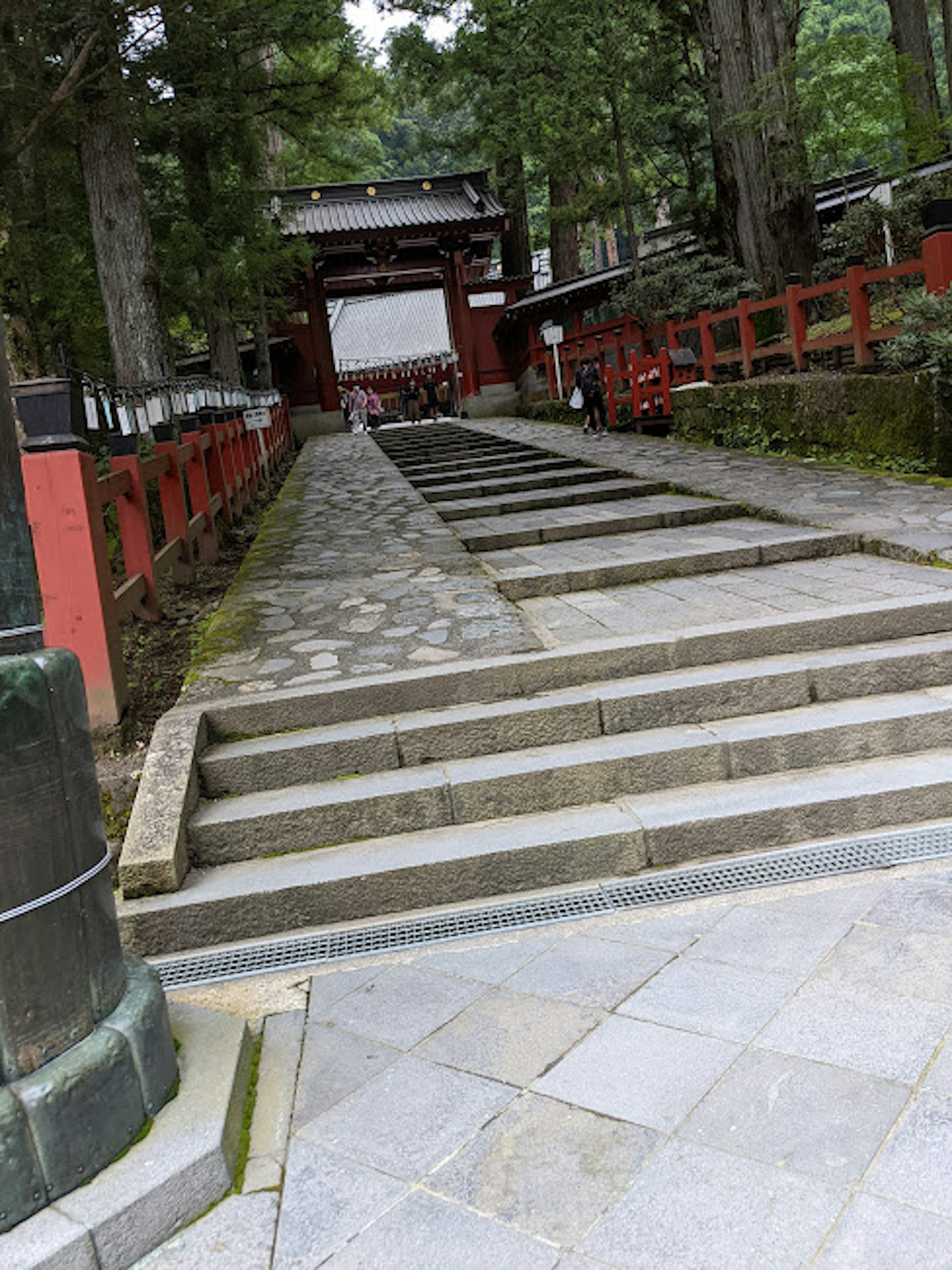 Escalier de pierre menant à l'entrée d'un sanctuaire entouré d'arbres verts et de clôtures rouges