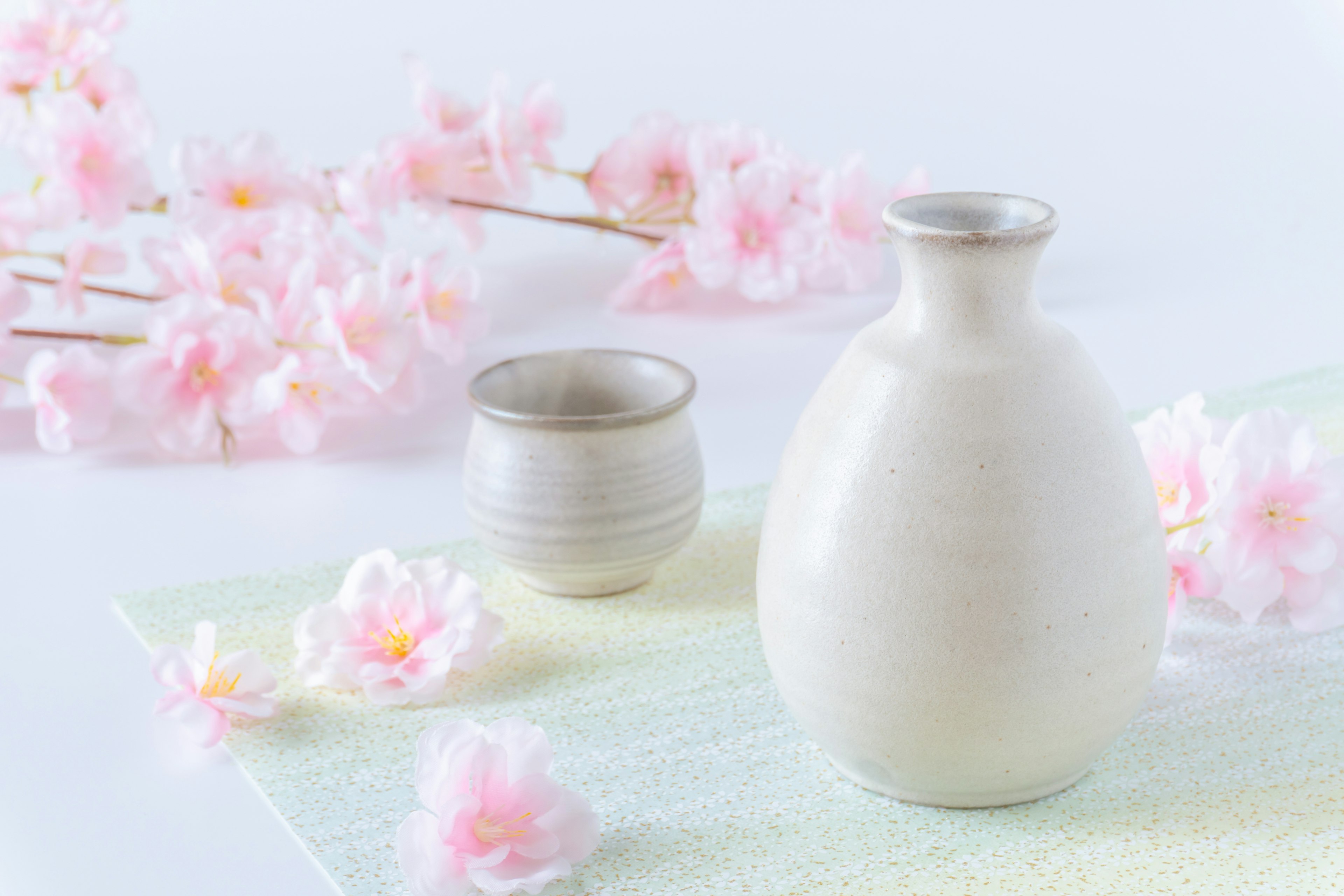 Naturaleza muerta de un jarrón de cerámica blanca y una taza rodeados de flores de cerezo