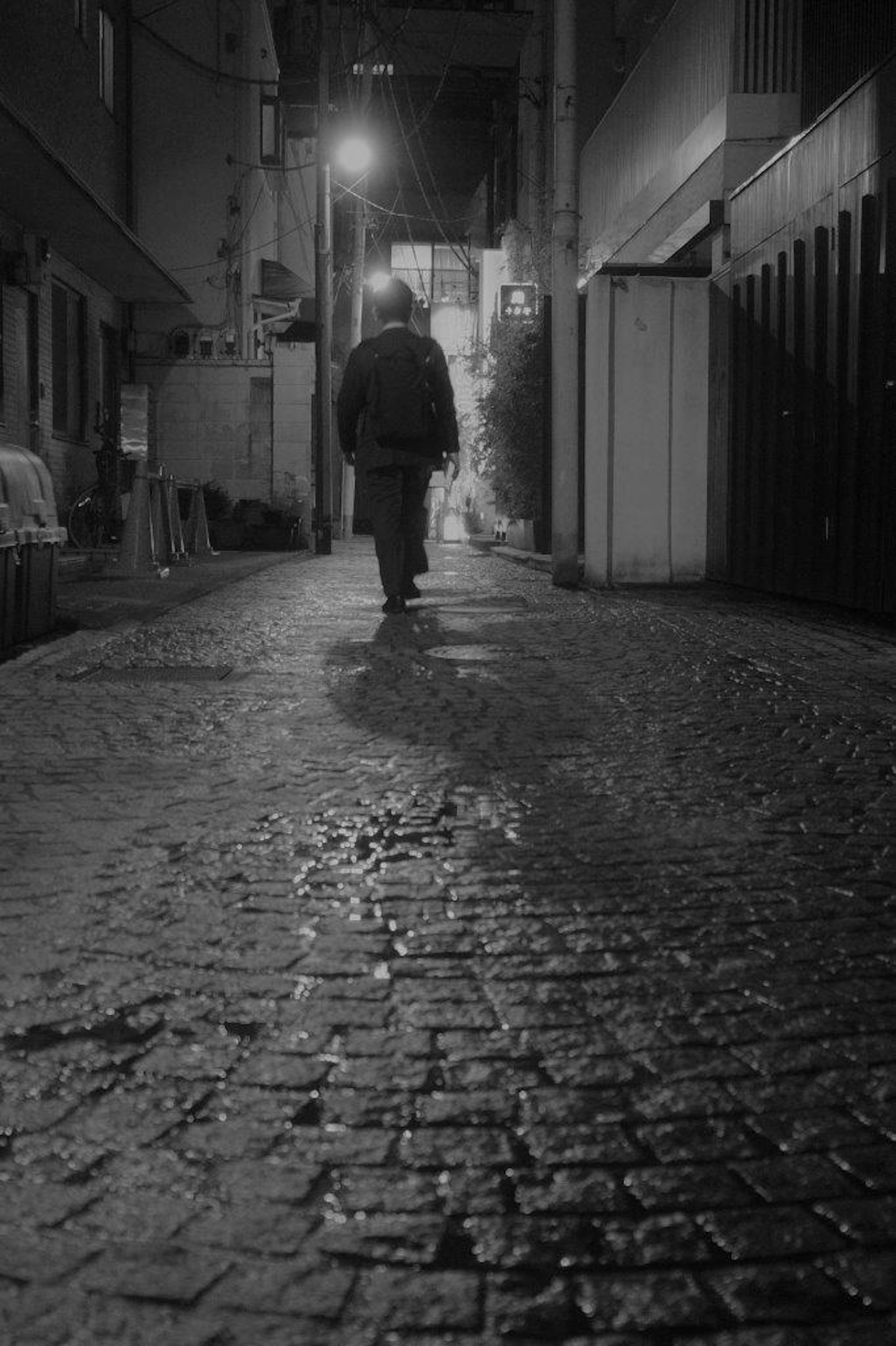 Silhouette d'une personne marchant dans une ruelle sombre avec des pavés