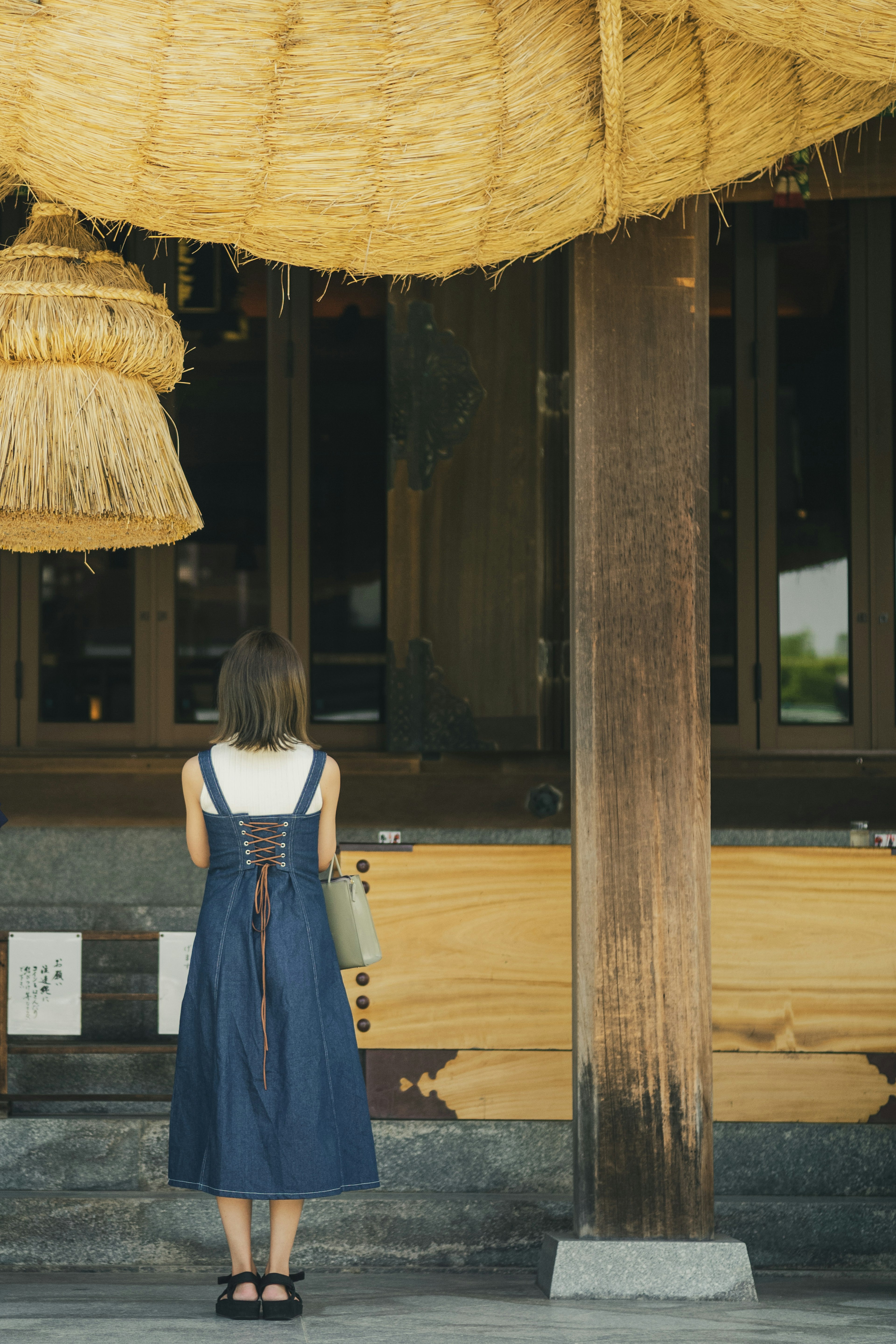 女性が藁の屋根の下で神社に向かって立っている