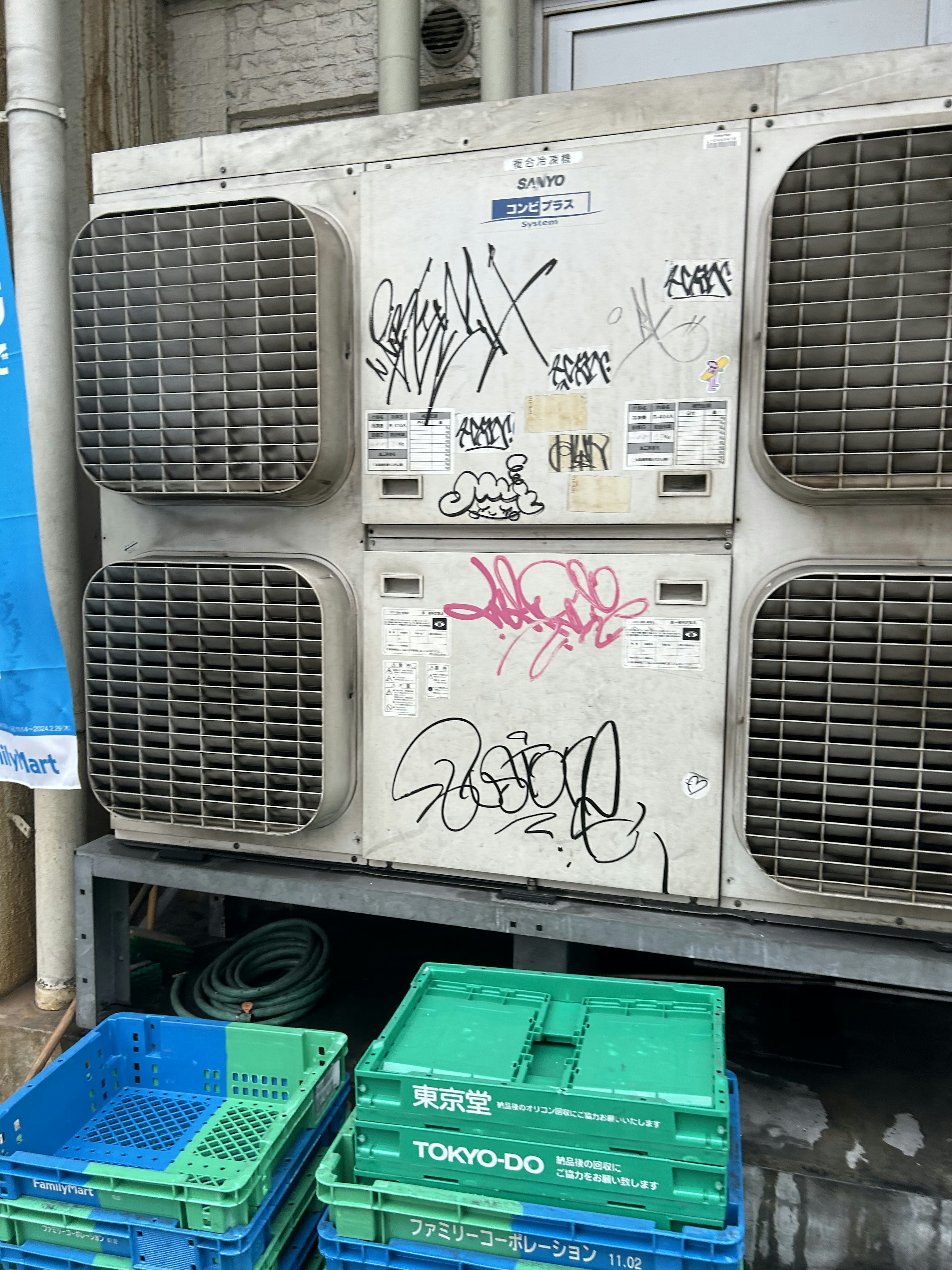 Unidad de aire acondicionado vieja con graffiti y cajas de plástico azules debajo